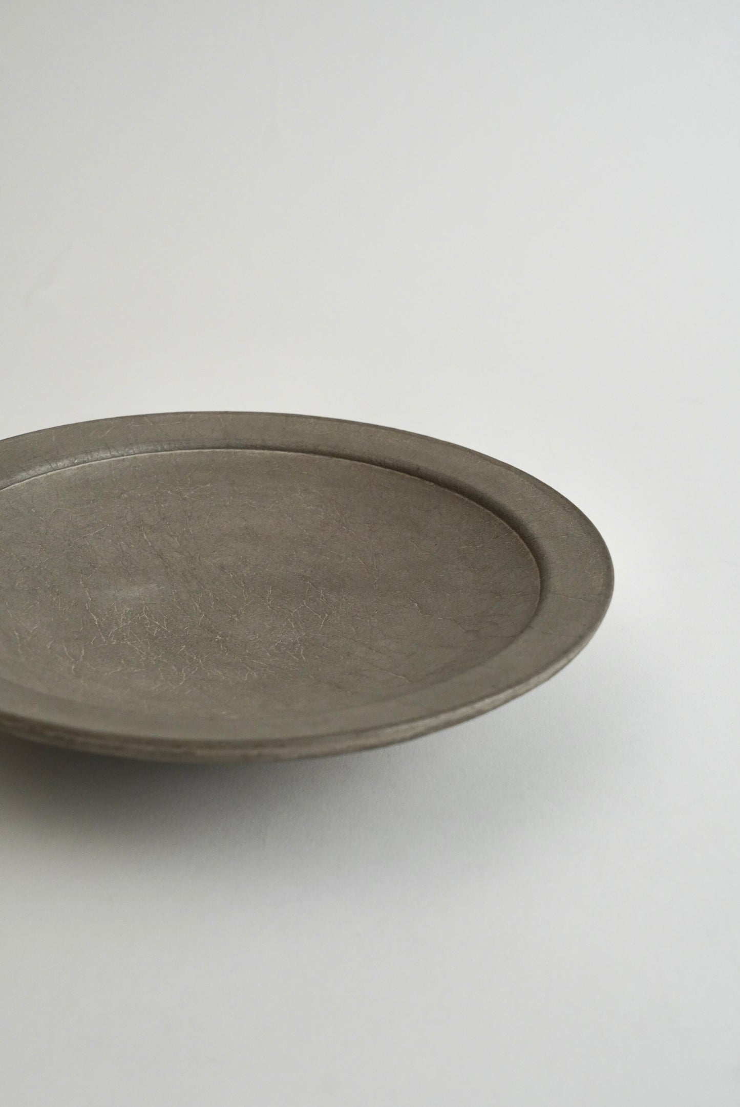 A minimalist, round ceramic tray or shallow dish with a matte, textured gray finish, photographed on a clean, light gray background.