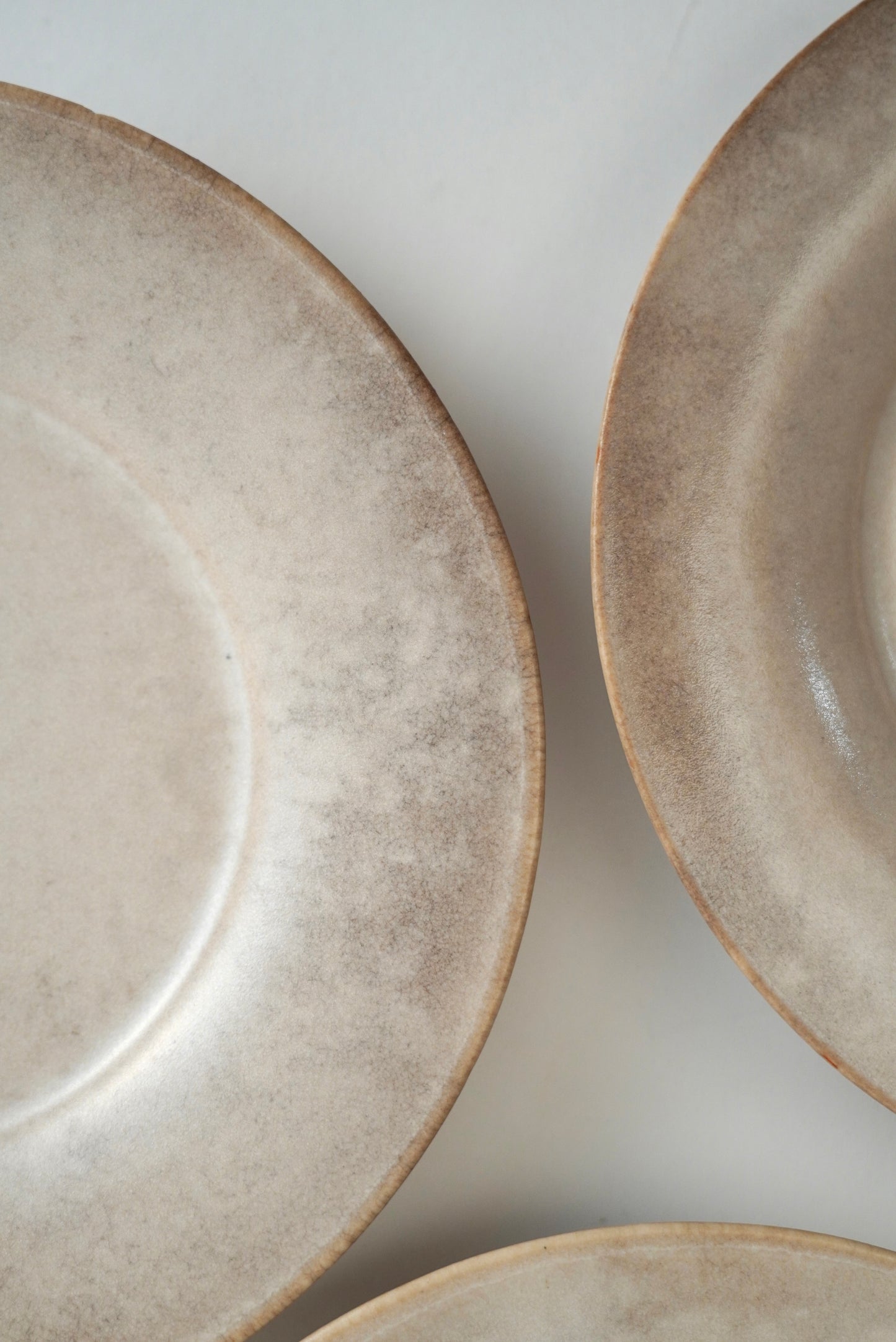 Close-up of ceramic plates with a textured, speckled beige and light brown glaze on a neutral off-white background.