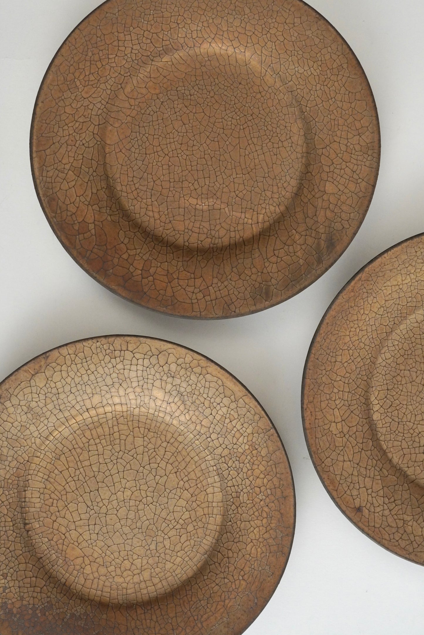 Three round ceramic plates with a brown crackle glaze, arranged diagonally on a white background.