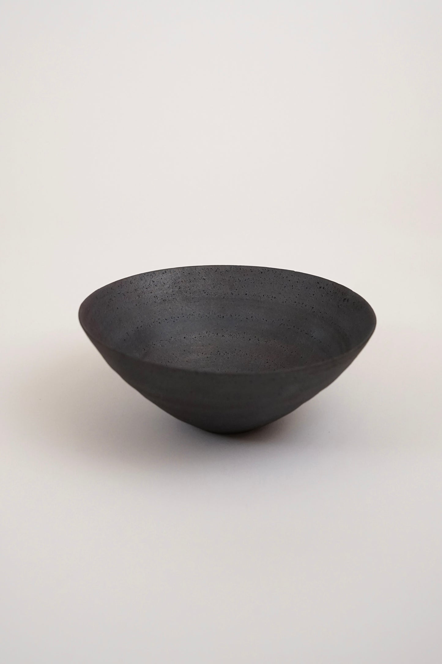 A dark charcoal gray ceramic bowl with a textured, speckled finish, photographed on a clean, light gray studio background.