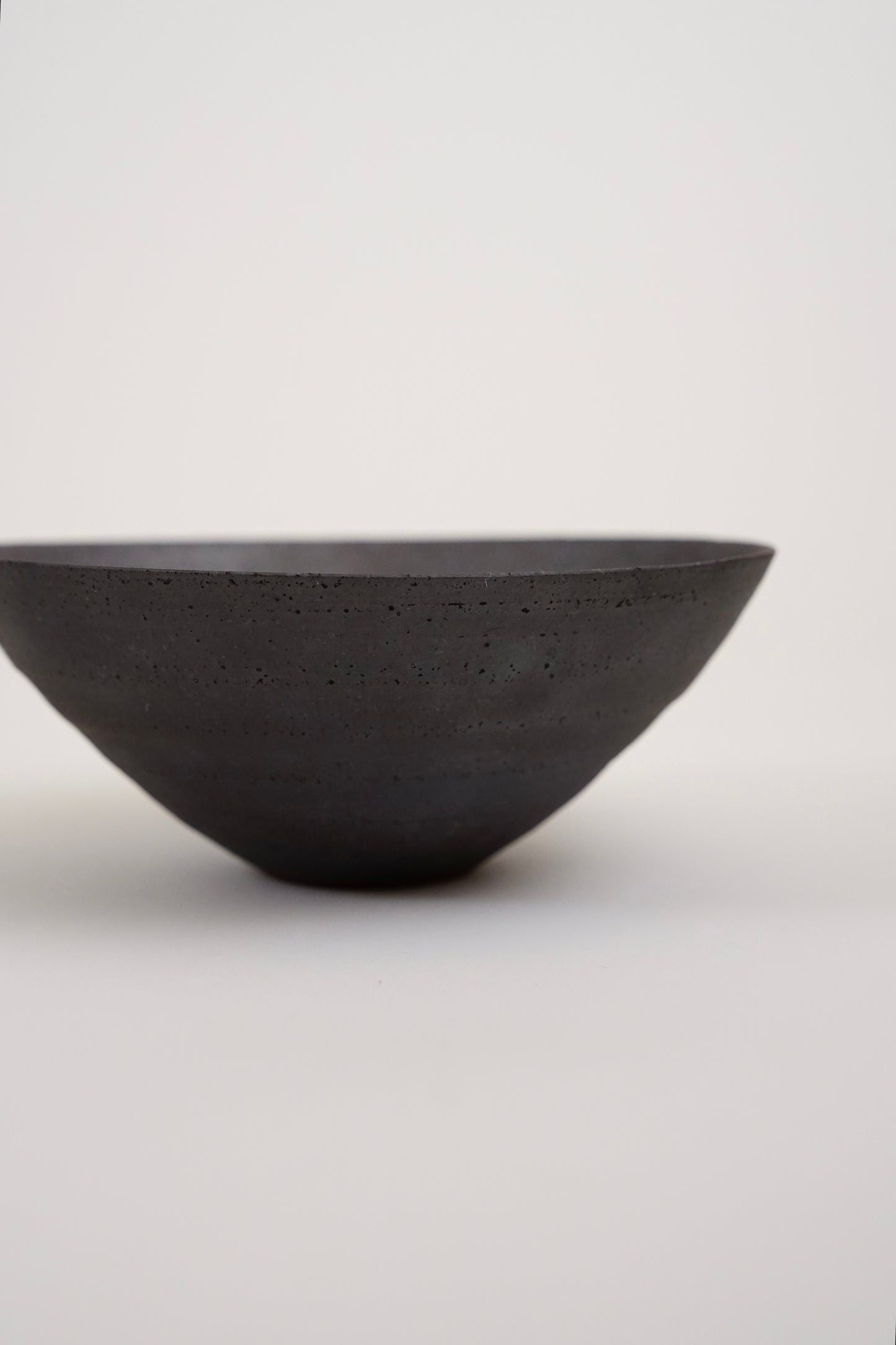 A dark charcoal gray concrete bowl with a textured matte finish, photographed against a seamless light gray background.
