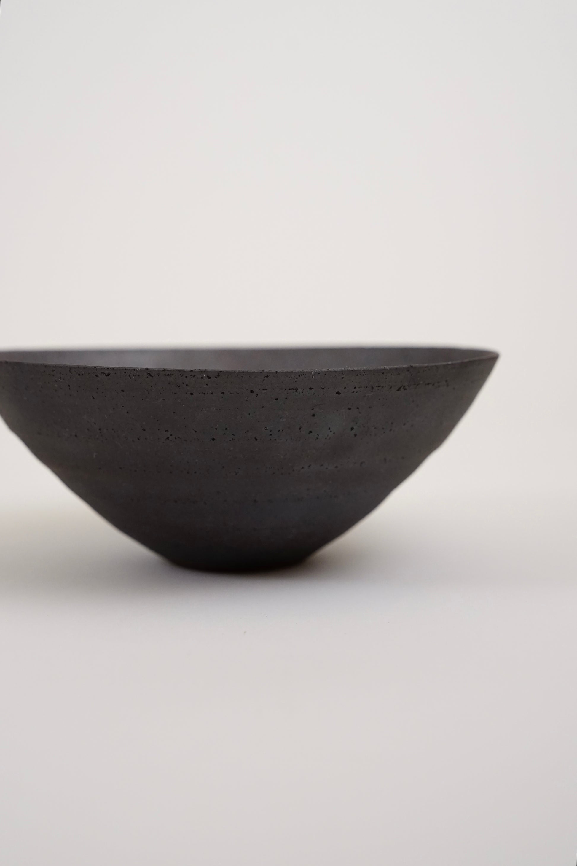 A dark charcoal gray concrete bowl with a textured matte finish, photographed against a seamless light gray background.