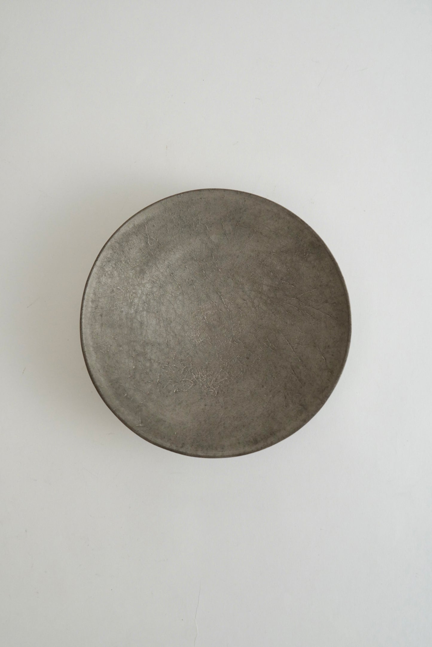 A round, shallow metal tray or dish with a textured, matte gray finish, photographed from directly above on a plain white background.
