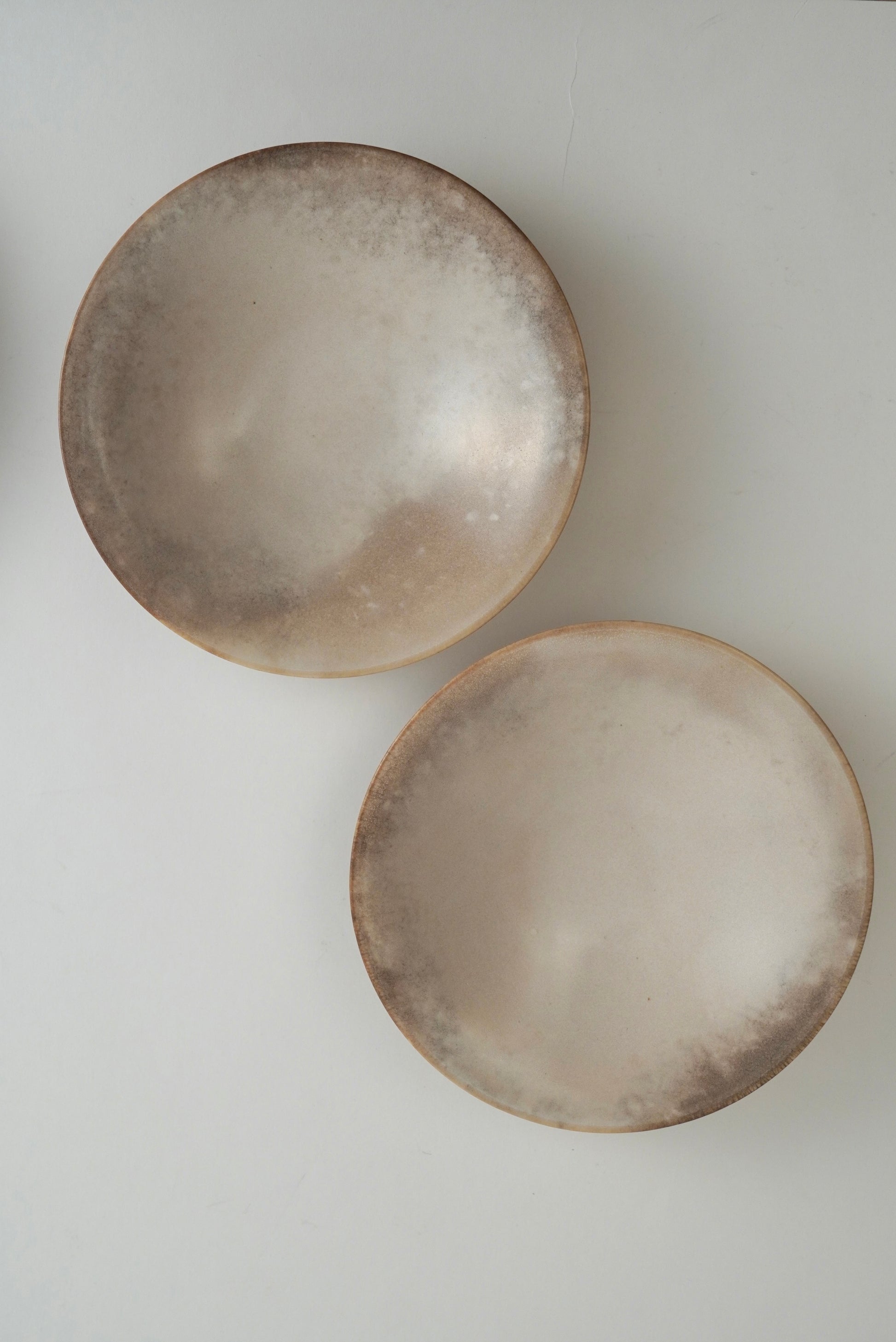 Two round ceramic bowls with a mottled, organic metallic finish in champagne gold and bronze tones, photographed on a light gray background.