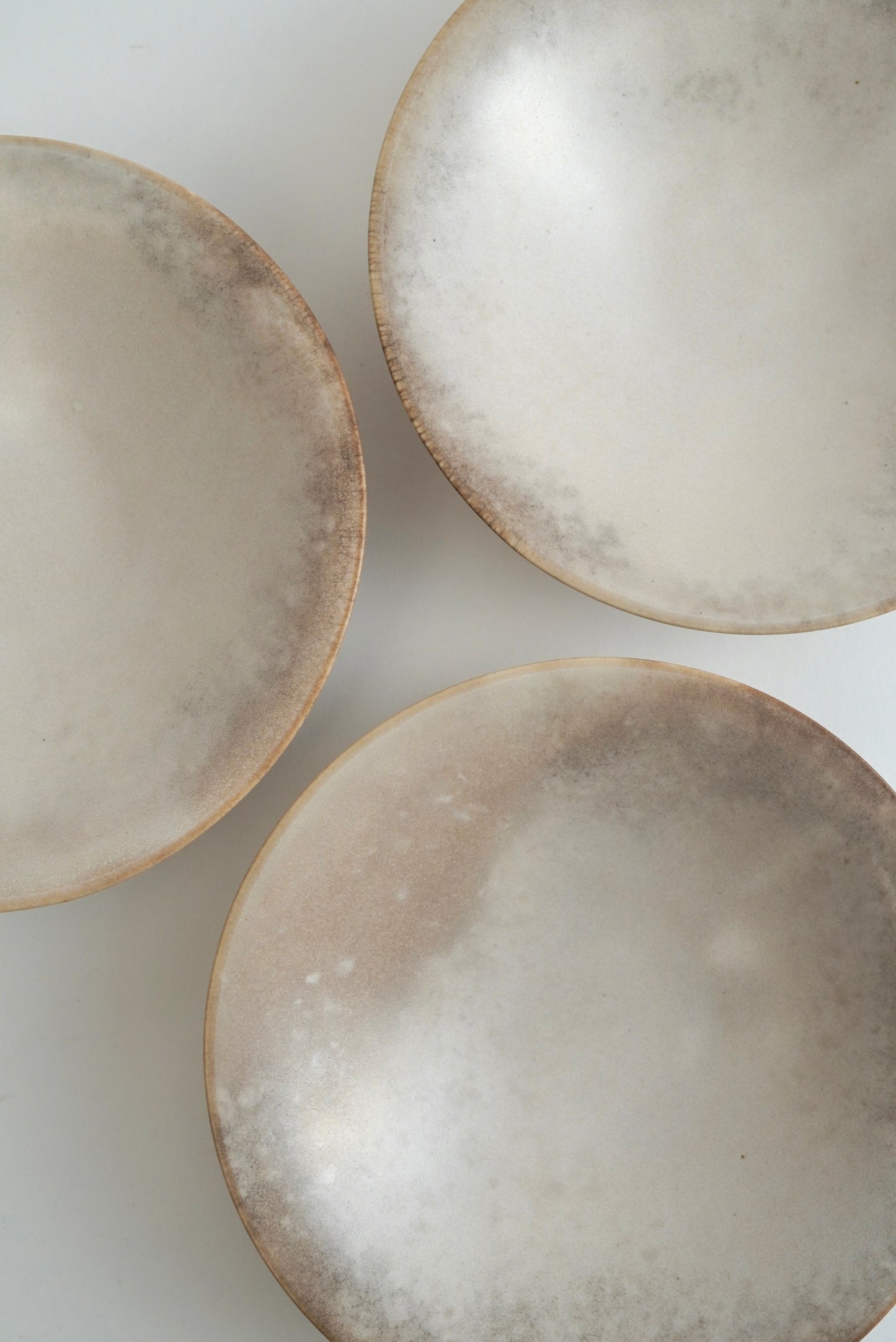 Three shallow round ceramic bowls with a textured, speckled beige and white glaze, arranged on a plain white surface.