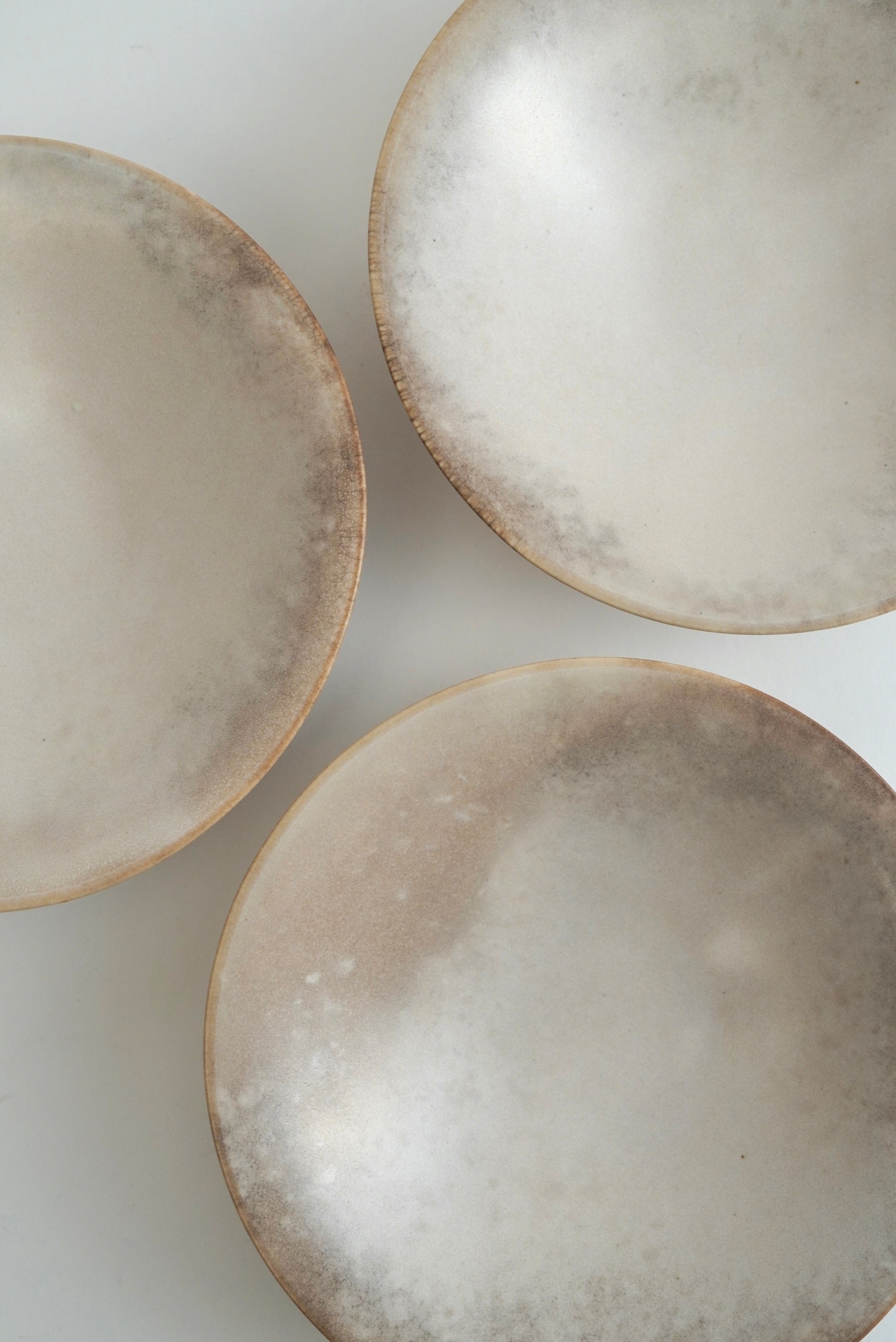 Three shallow round ceramic bowls with a textured, speckled beige and white glaze, arranged on a plain white surface.