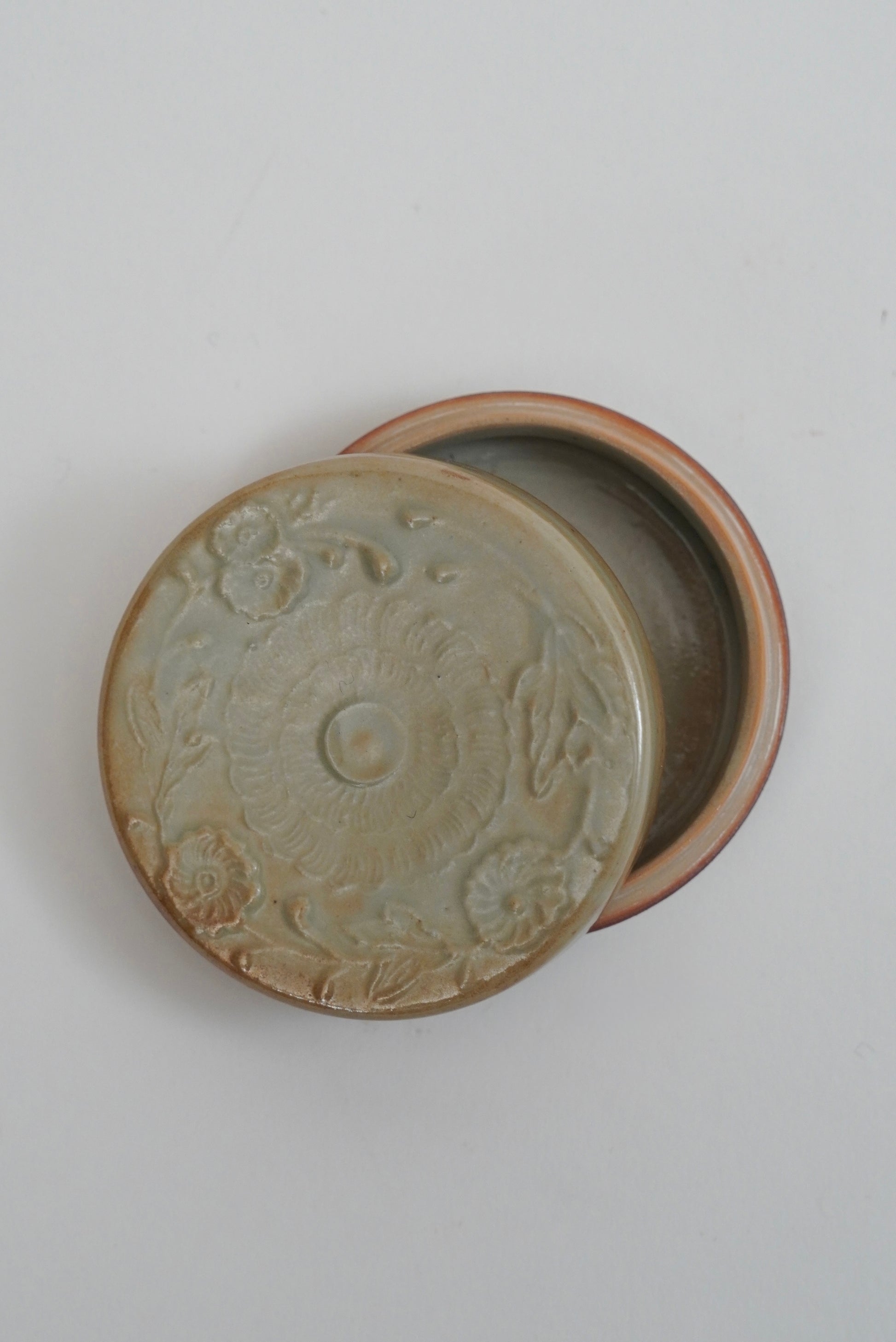 An antique ceramic lidded box with a floral embossed design on the lid and a reddish-brown rim, shown open against a plain light background.