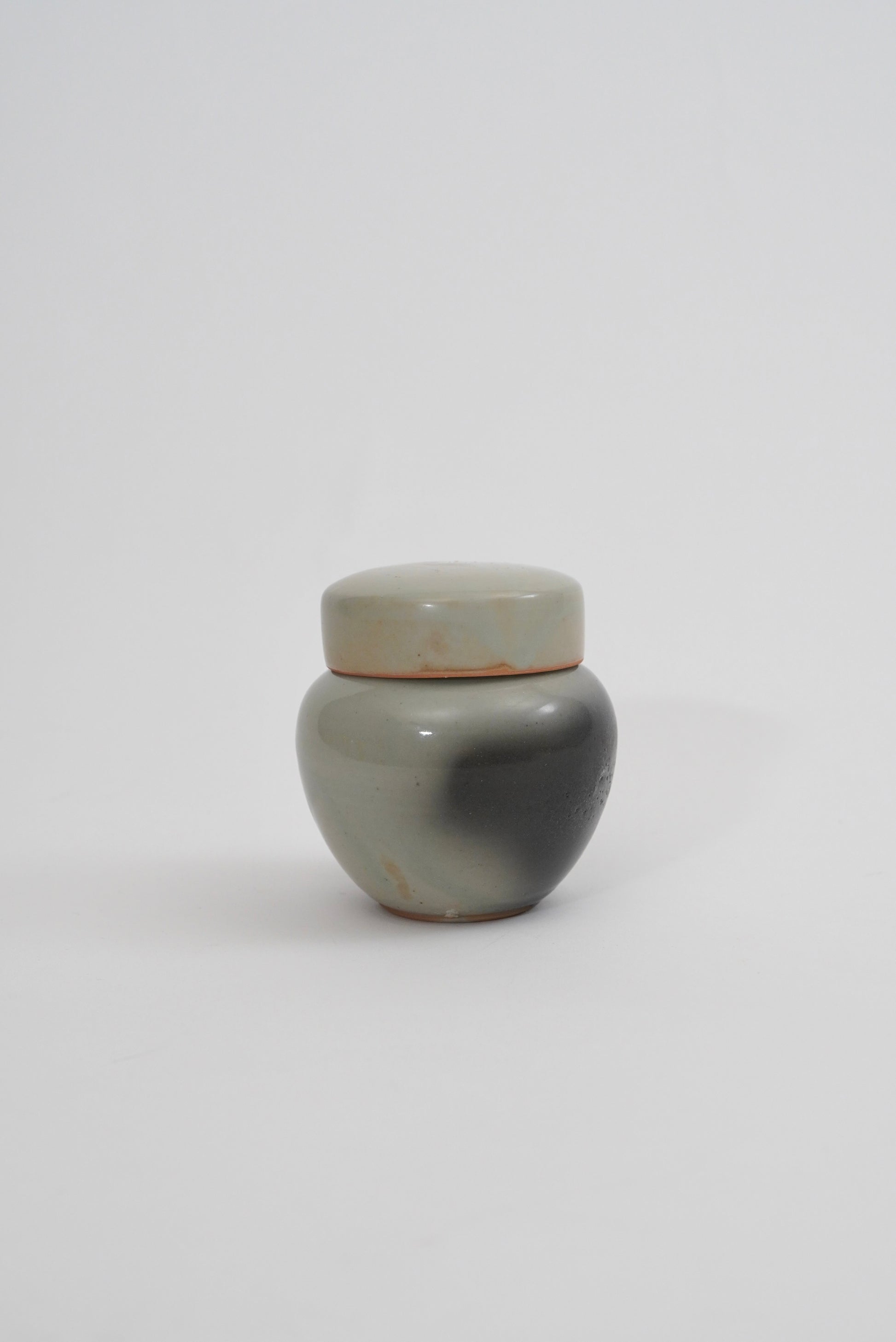 A small round ceramic jar with a matching lid, featuring a marbled finish in shades of gray, black, and beige, set against a plain light gray background.