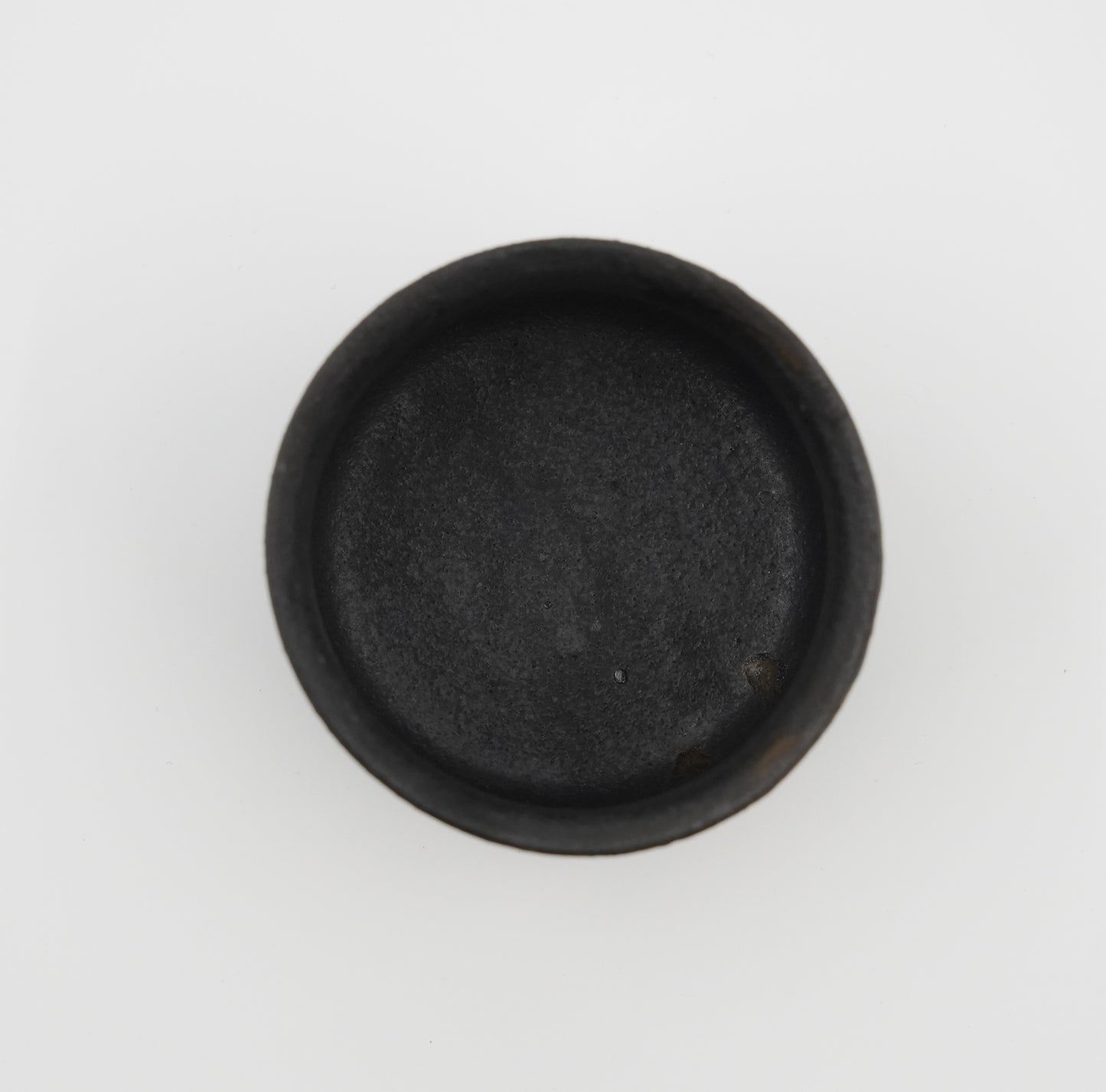 Black round object on a white background. Handmade ceramic cup by Japanese artist at Gallery tete Hong Kong.
