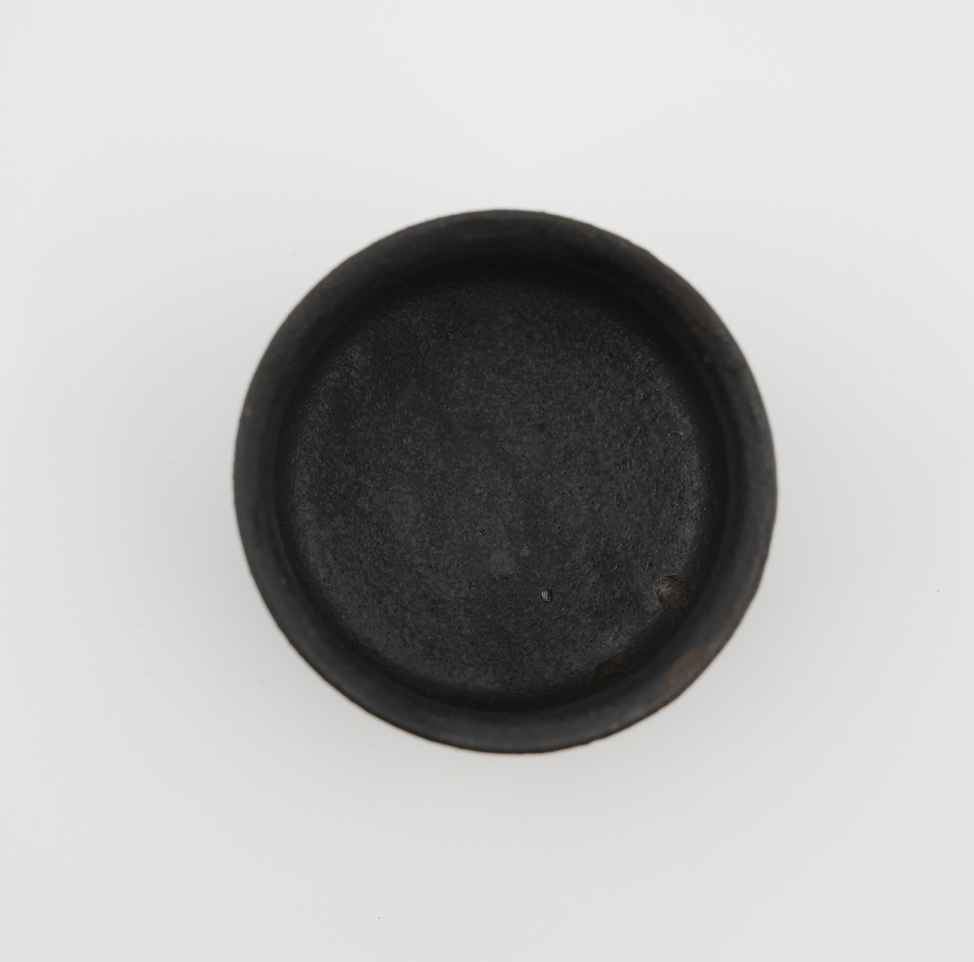 Black round object on a white background. Handmade ceramic cup by Japanese artist at Gallery tete Hong Kong.