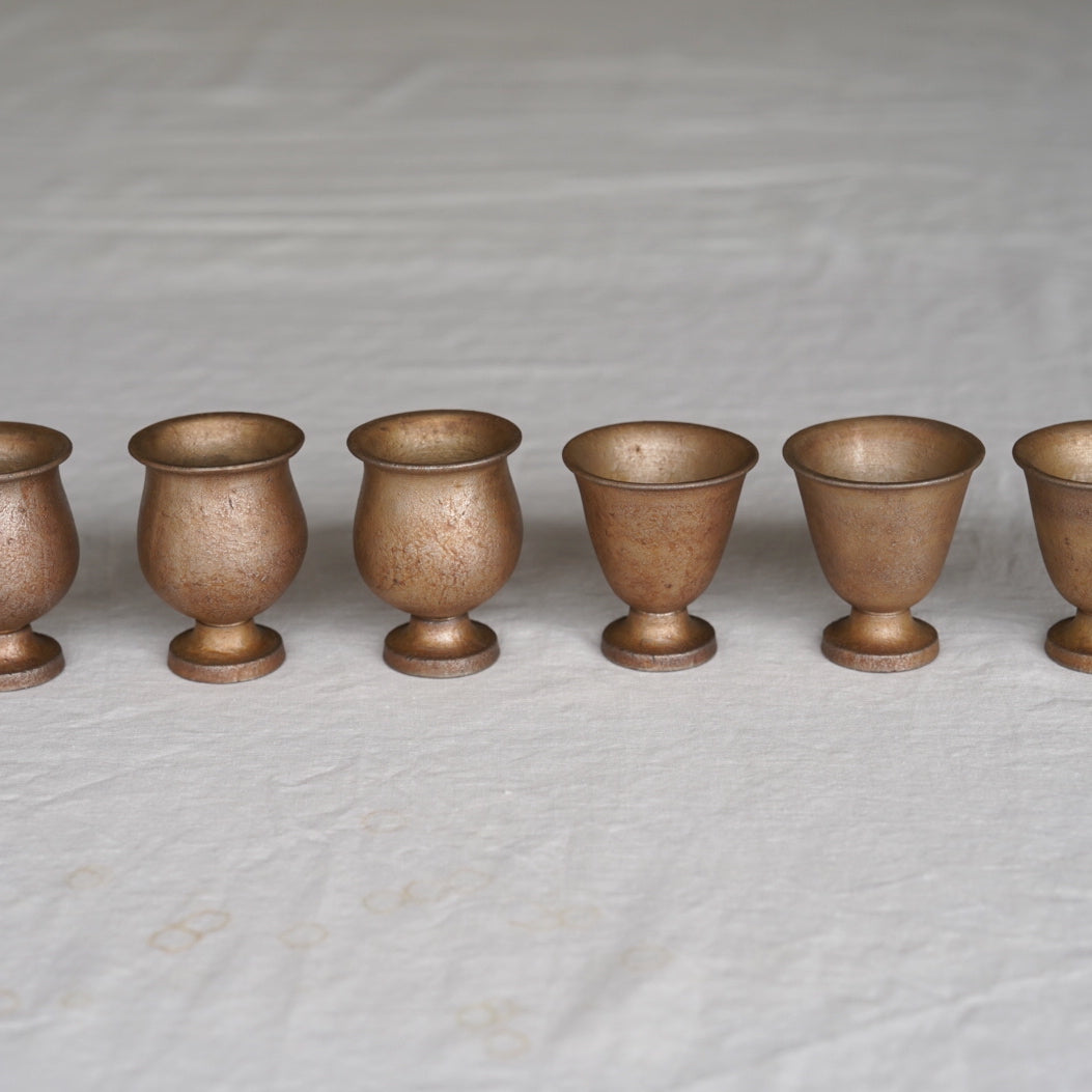 Row of six bronze goblets on a textured gray surface. Handmade ceramic cup by Japanese artist at Gallery tete Hong Kong.