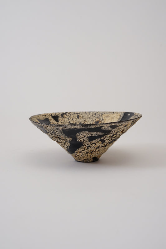A small decorative bowl with a black base and extensive textured gold leaf pattern, photographed on a neutral light gray background.