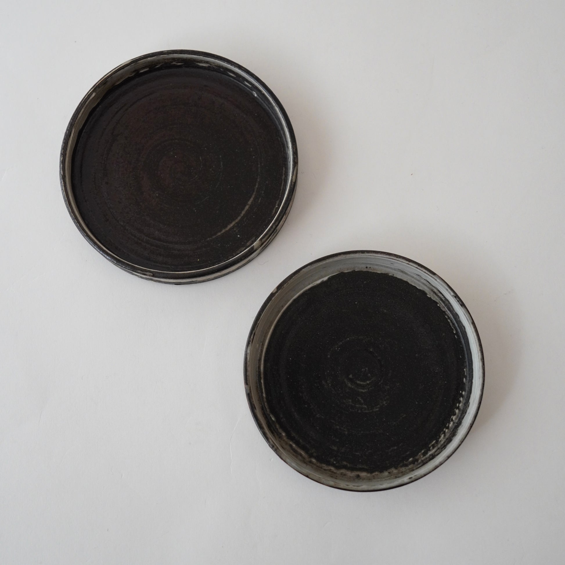 Two black Hakeme ceramic small plate on white surface. Handmade ceramic  plate by Japanese artist at Gallery tete Hong Kong.