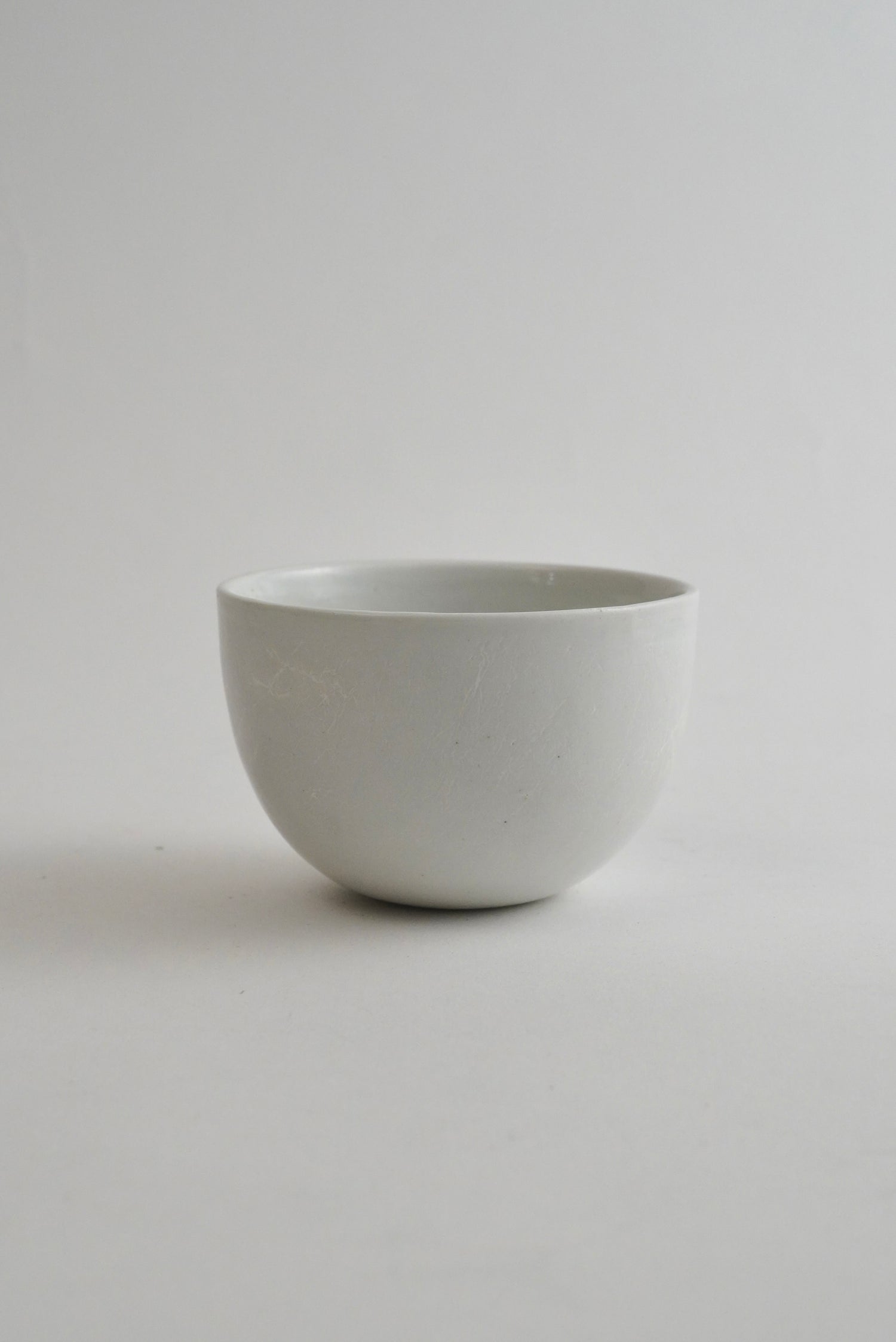 A minimalist, matte white ceramic bowl centered against a seamless light gray studio background.