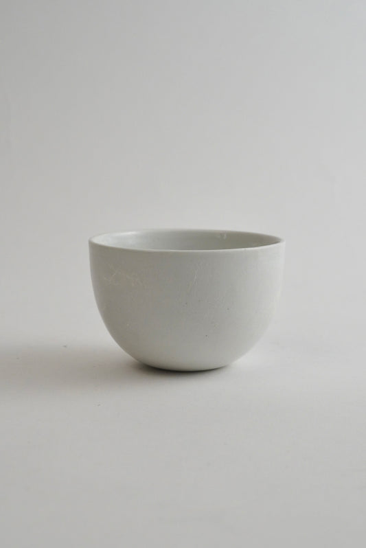 A minimalist, matte white ceramic bowl centered against a seamless light gray studio background.