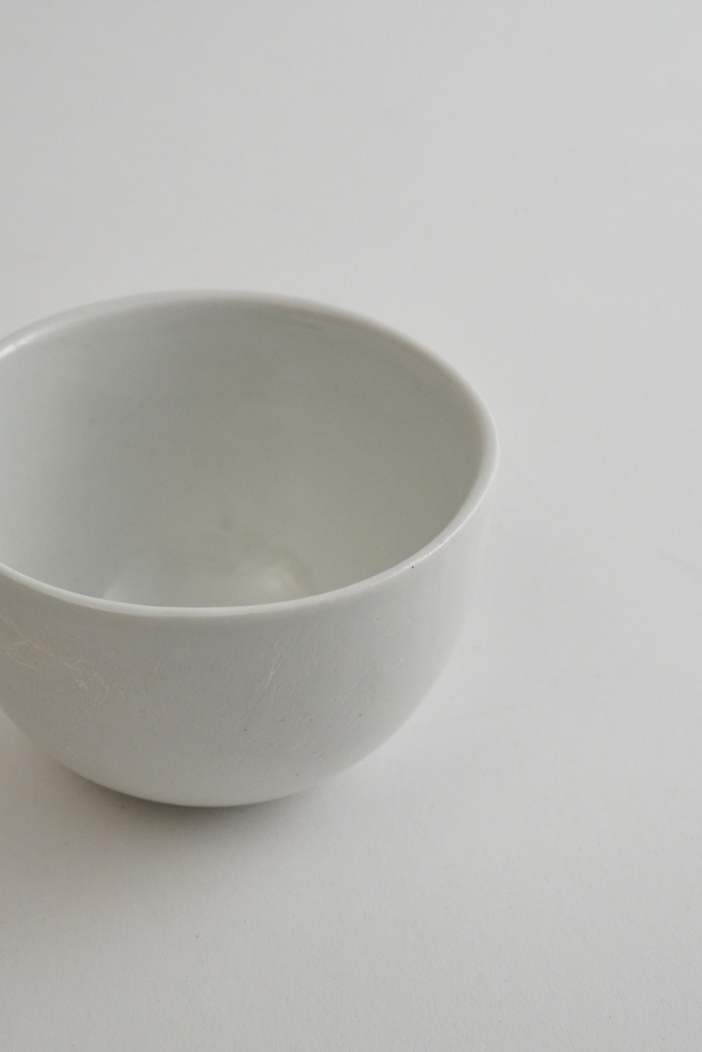 A minimalist white ceramic bowl with a smooth, matte finish, photographed from a high-angle perspective against a clean, light gray background.