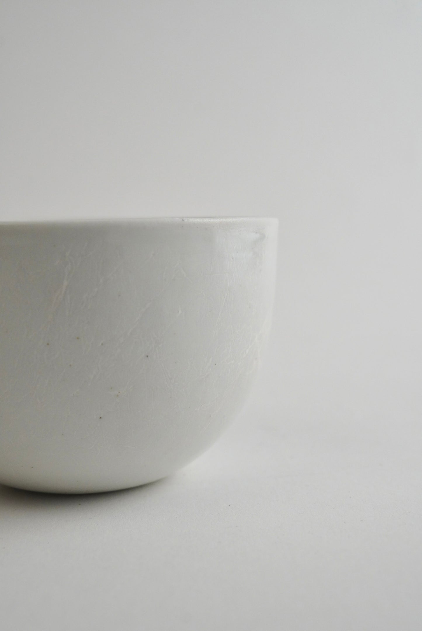 A close-up of a matte white ceramic bowl with a subtle speckled texture, set against a minimalist light gray background.