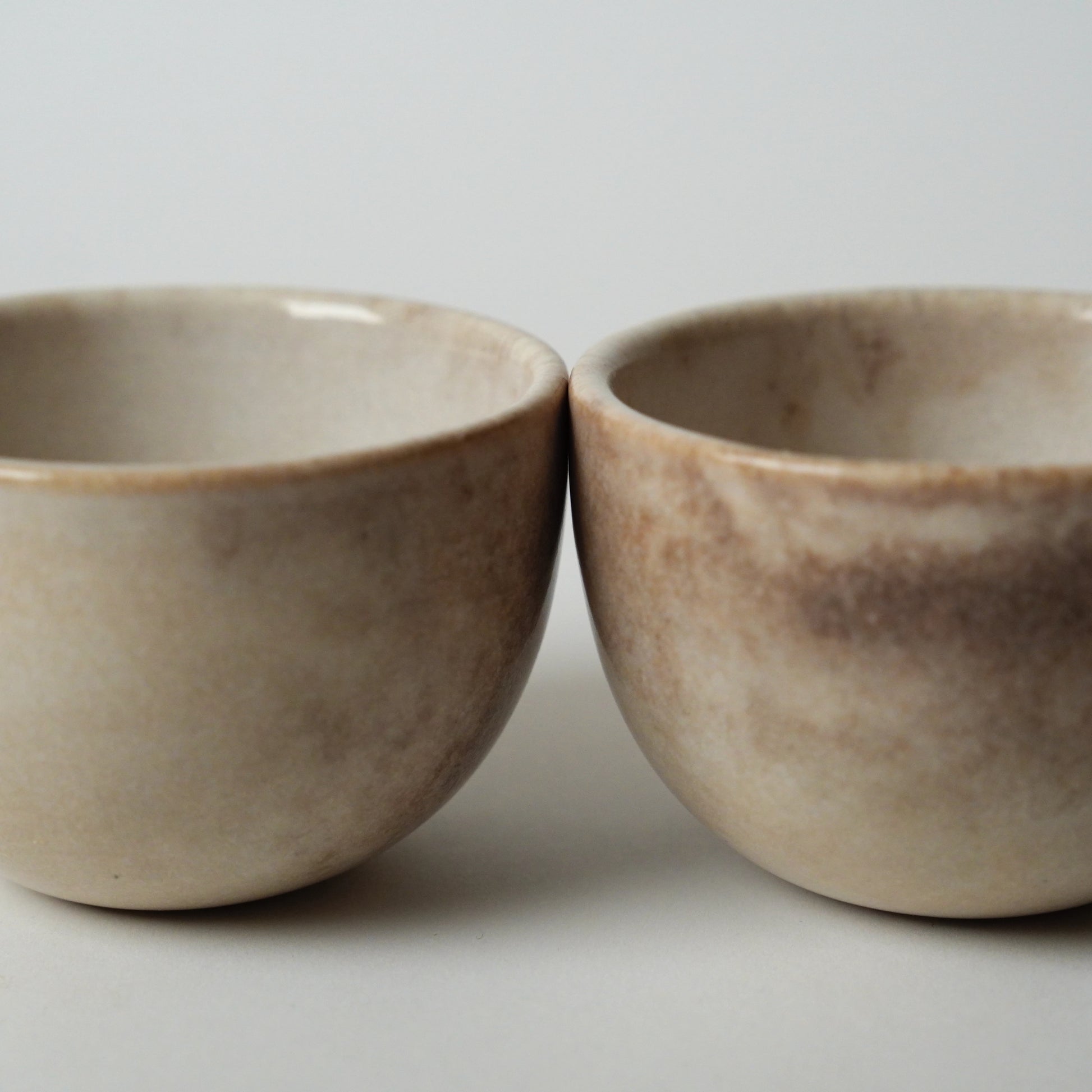 Two ceramic bowls with a mottled brown finish on a light gray background