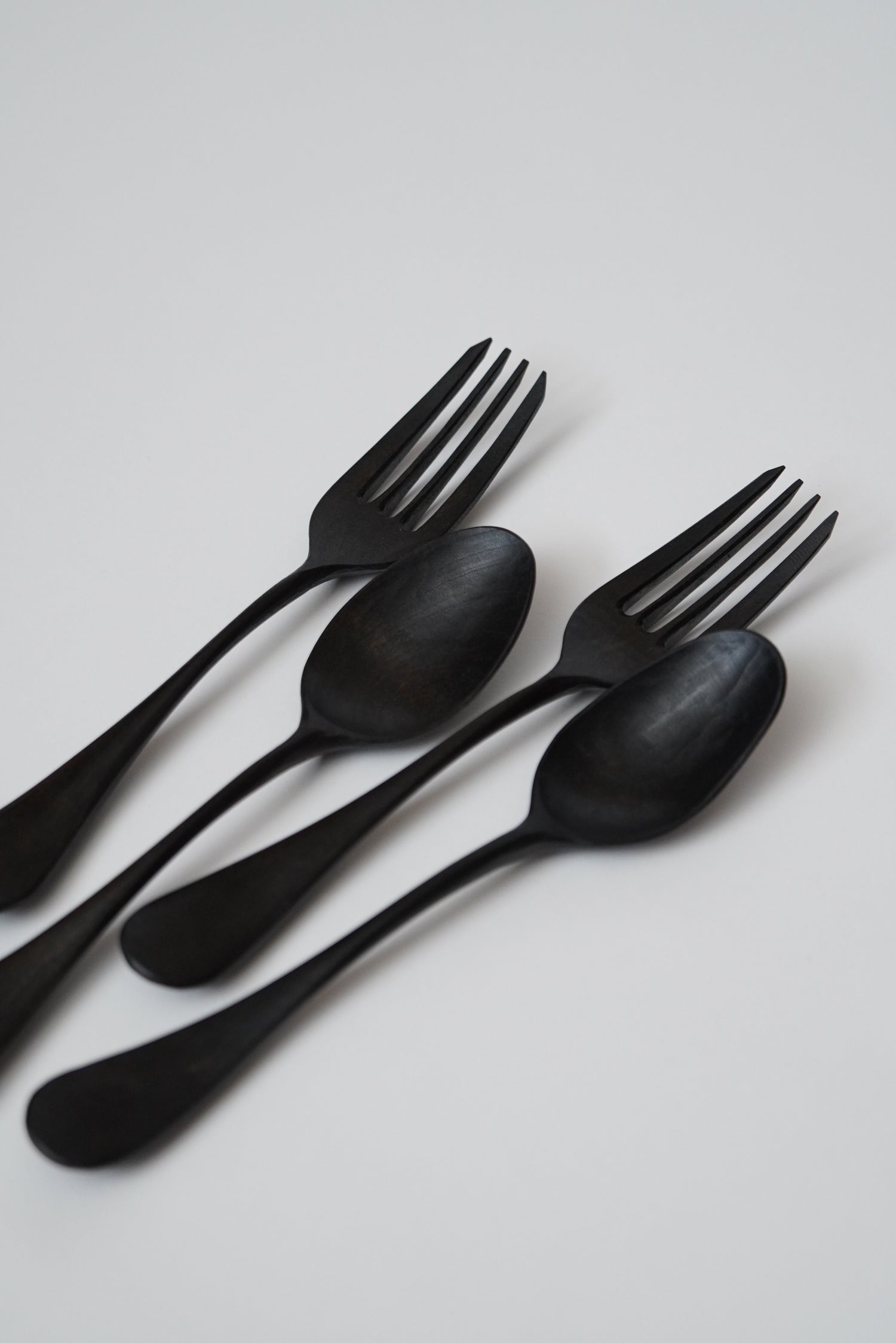 Set of black cutlery including spoons and forks on a light gray background