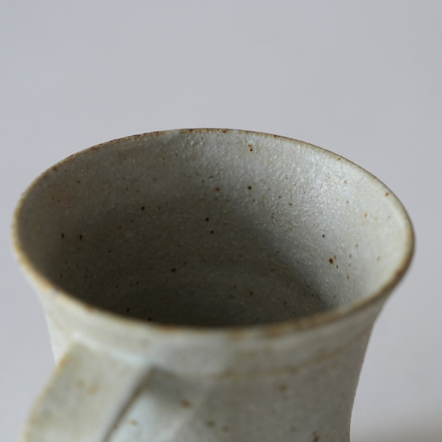 Close-up of a ceramic mug with a speckled texture on a light gray background