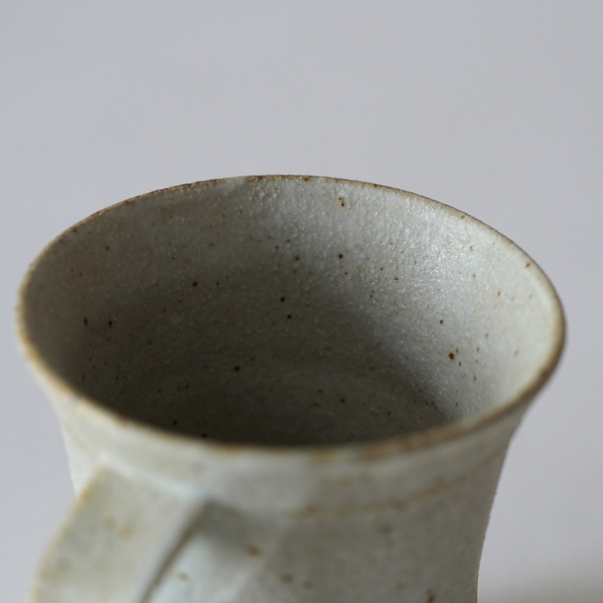 Close-up of a ceramic mug with a speckled texture on a light gray background