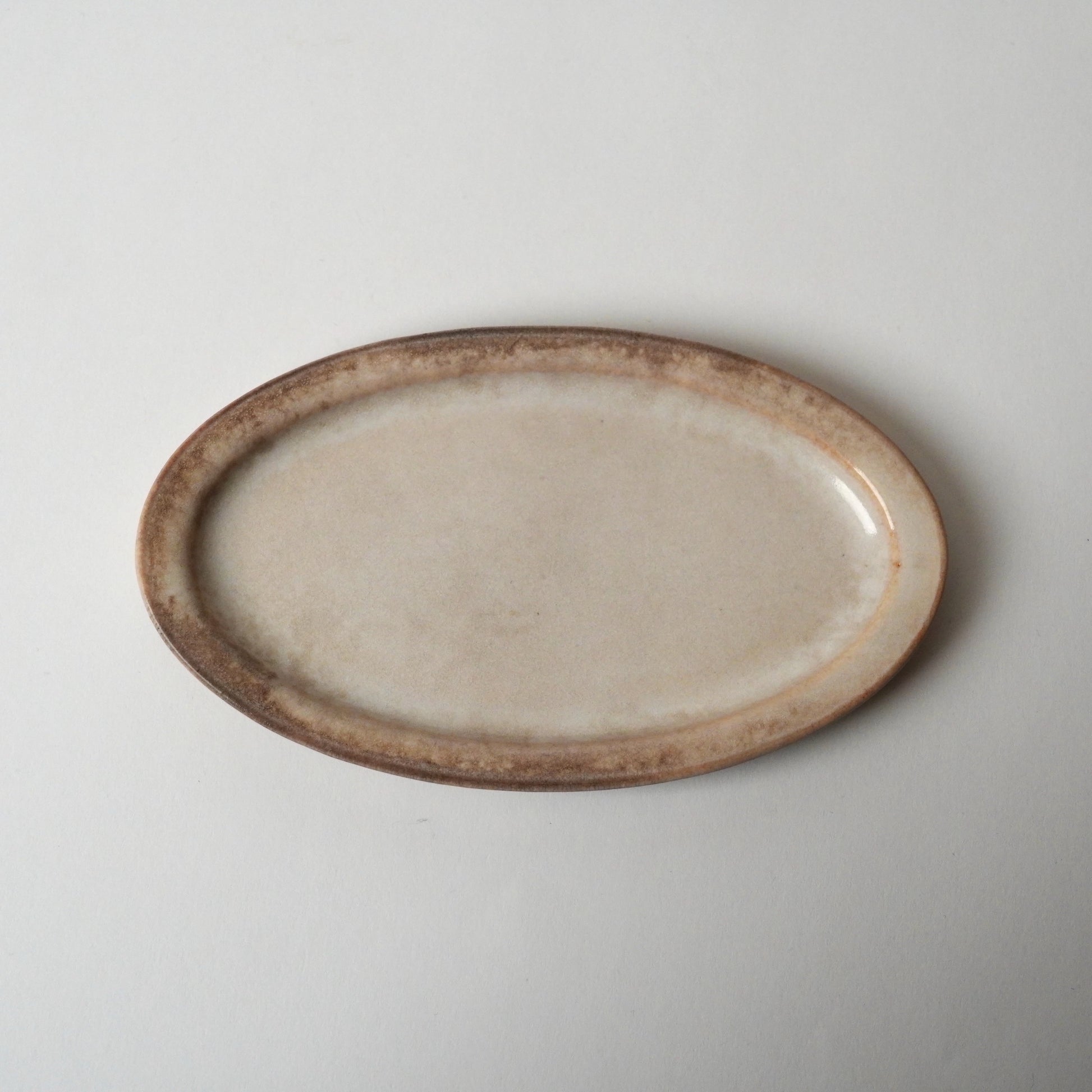 Oval ceramic plate with a rustic brown rim on a light gray background
