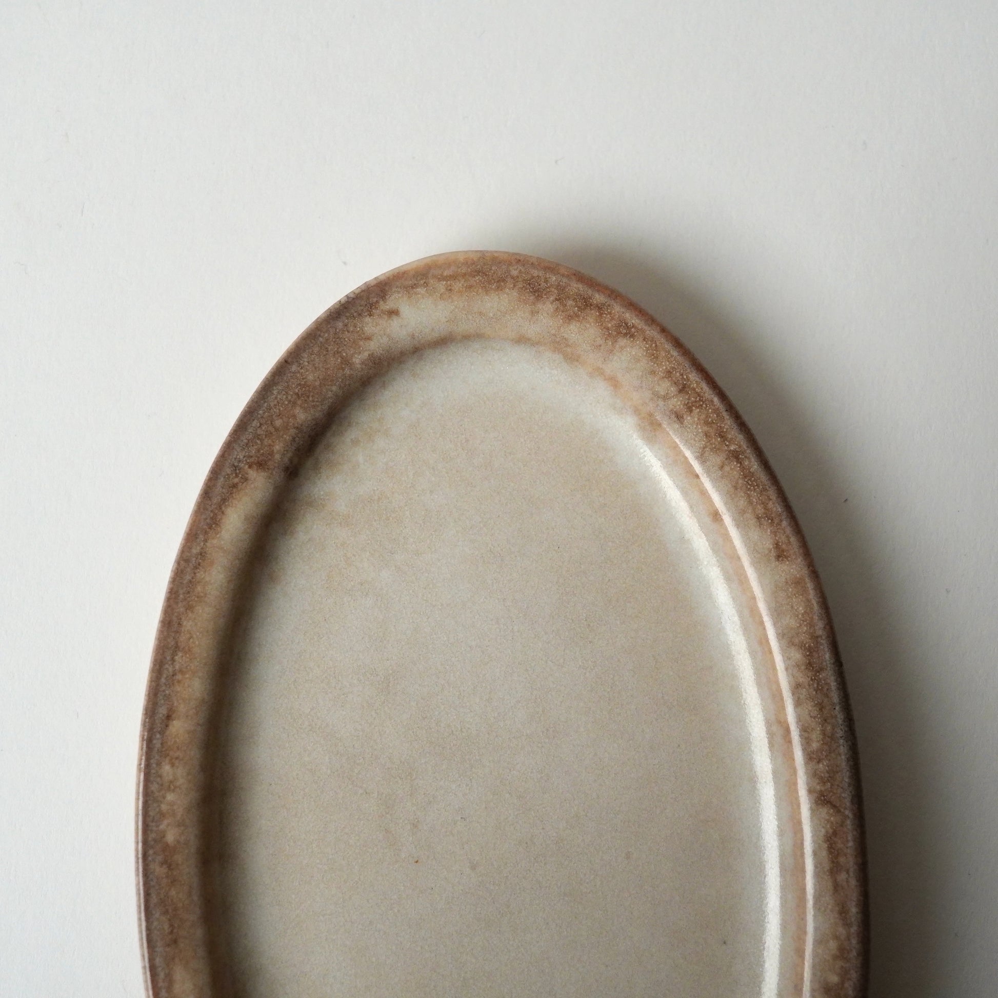 Oval ceramic plate with brown rim on a light gray background