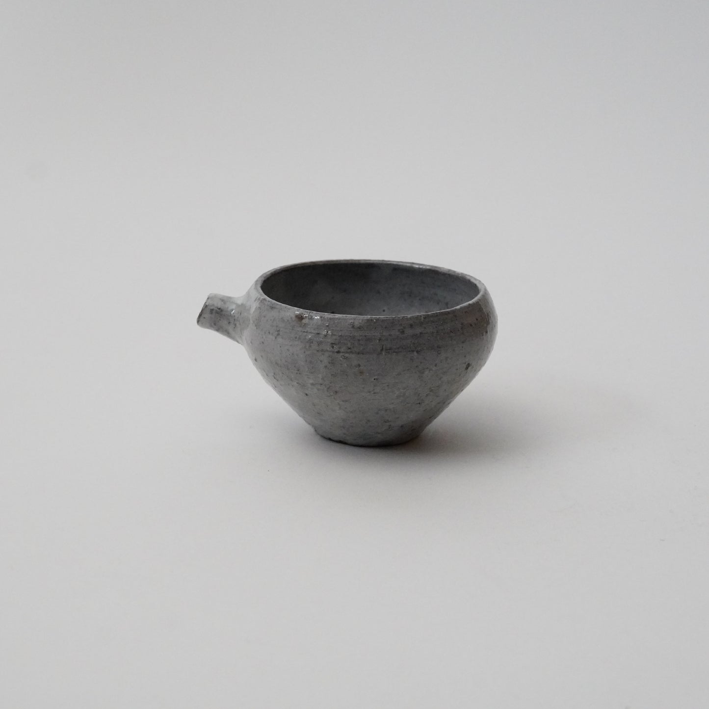 A gray ceramic pitcher with a round body and a spout on a white background.