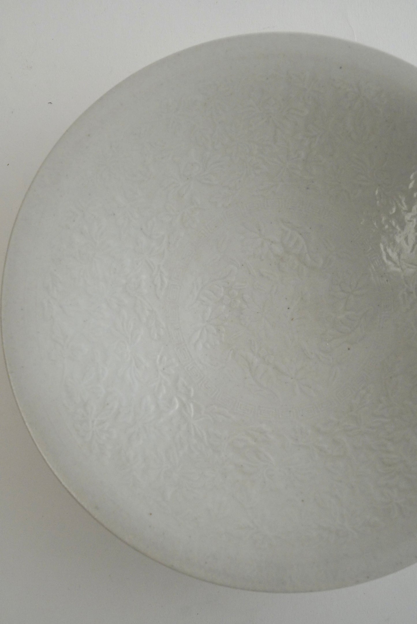 A close-up of a light gray textured glass bowl or dome, showing a subtle embossed floral pattern on a plain light background.