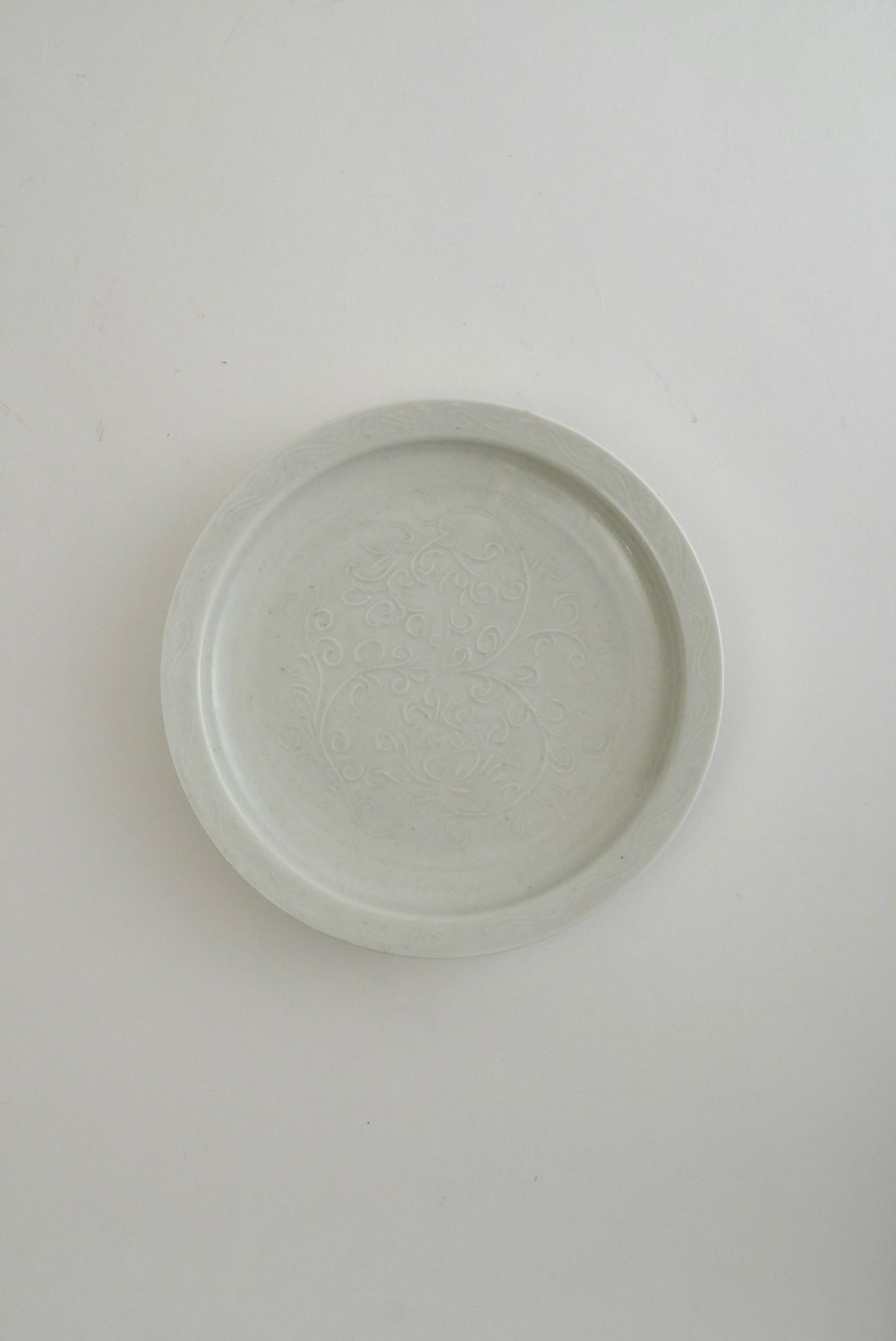 A round, shallow ceramic plate or dish with a subtle embossed floral pattern, shown from a top-down perspective on a plain white background.