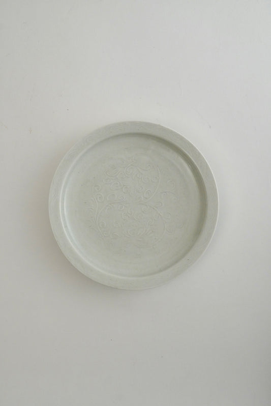 A round, shallow ceramic plate or dish with a subtle embossed floral pattern, shown from a top-down perspective on a plain white background.