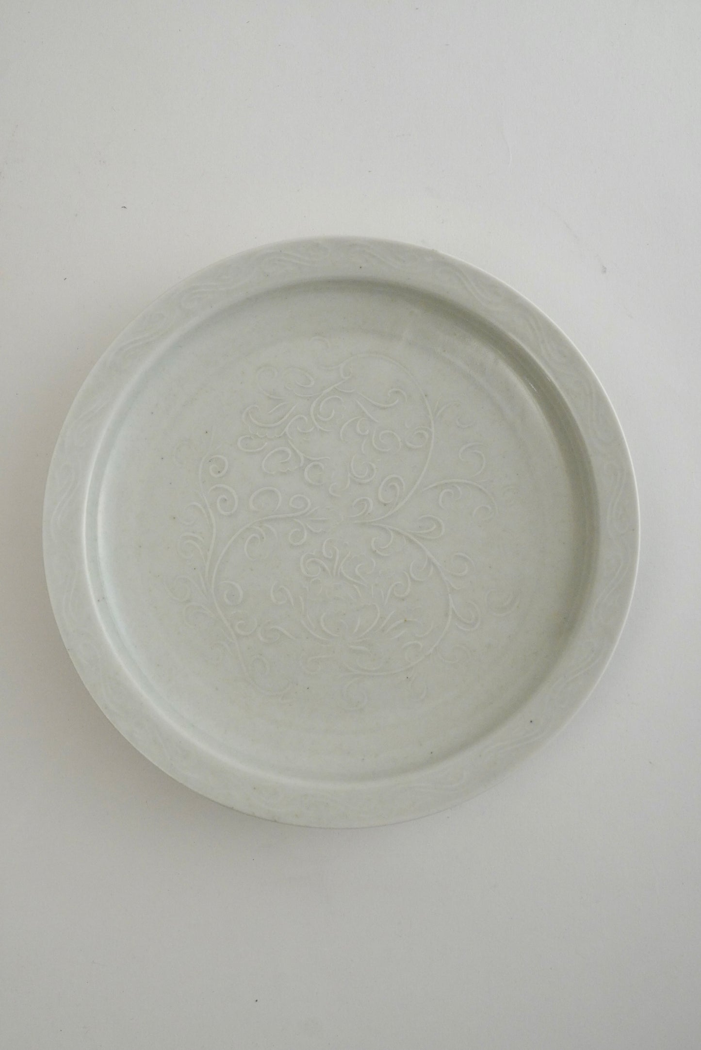 A round, shallow ceramic plate or dish with a subtle embossed floral pattern, shown from a top-down perspective on a plain white background.