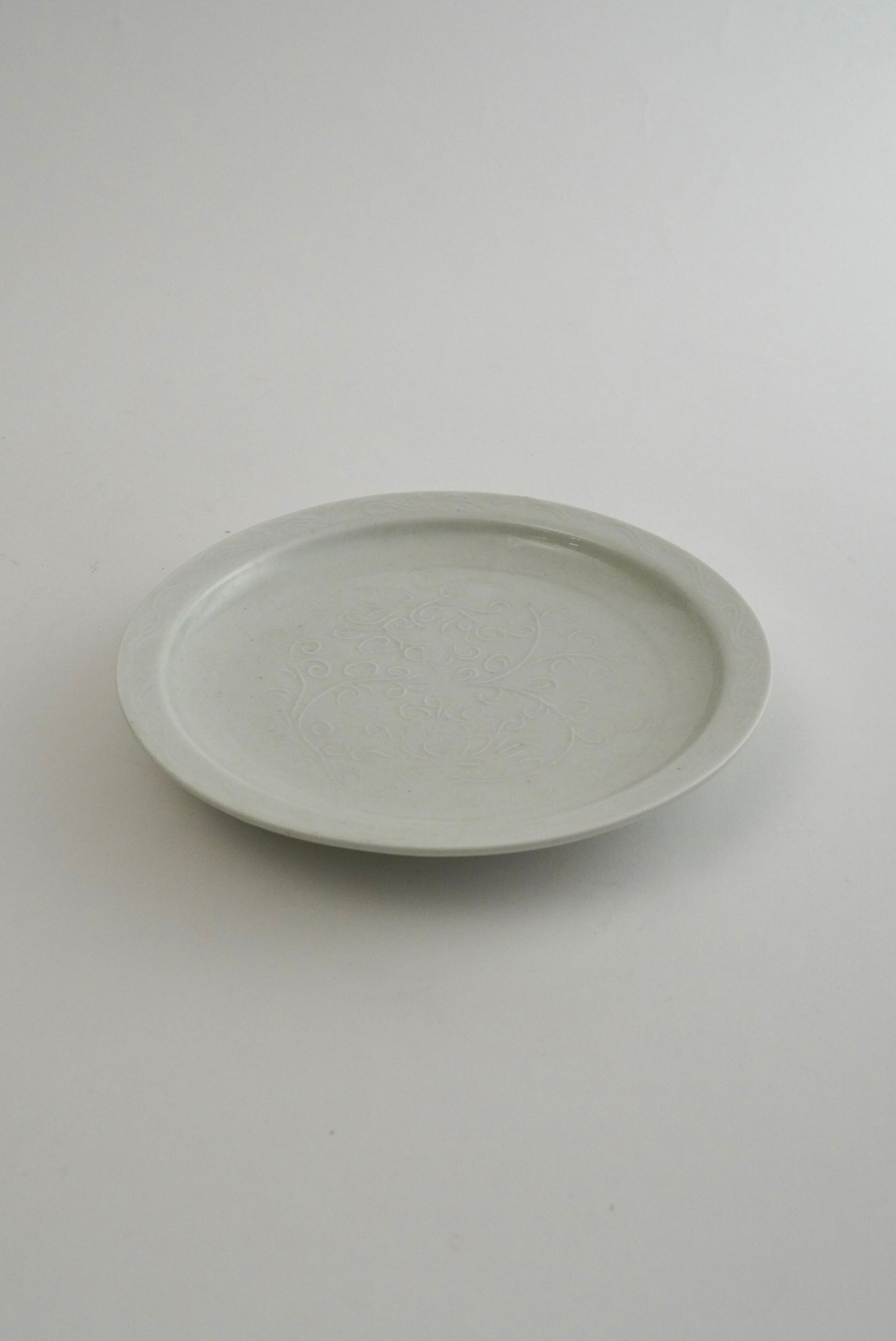 A round ceramic plate with a subtle textured glaze, photographed from a top-down perspective on a neutral light gray background.