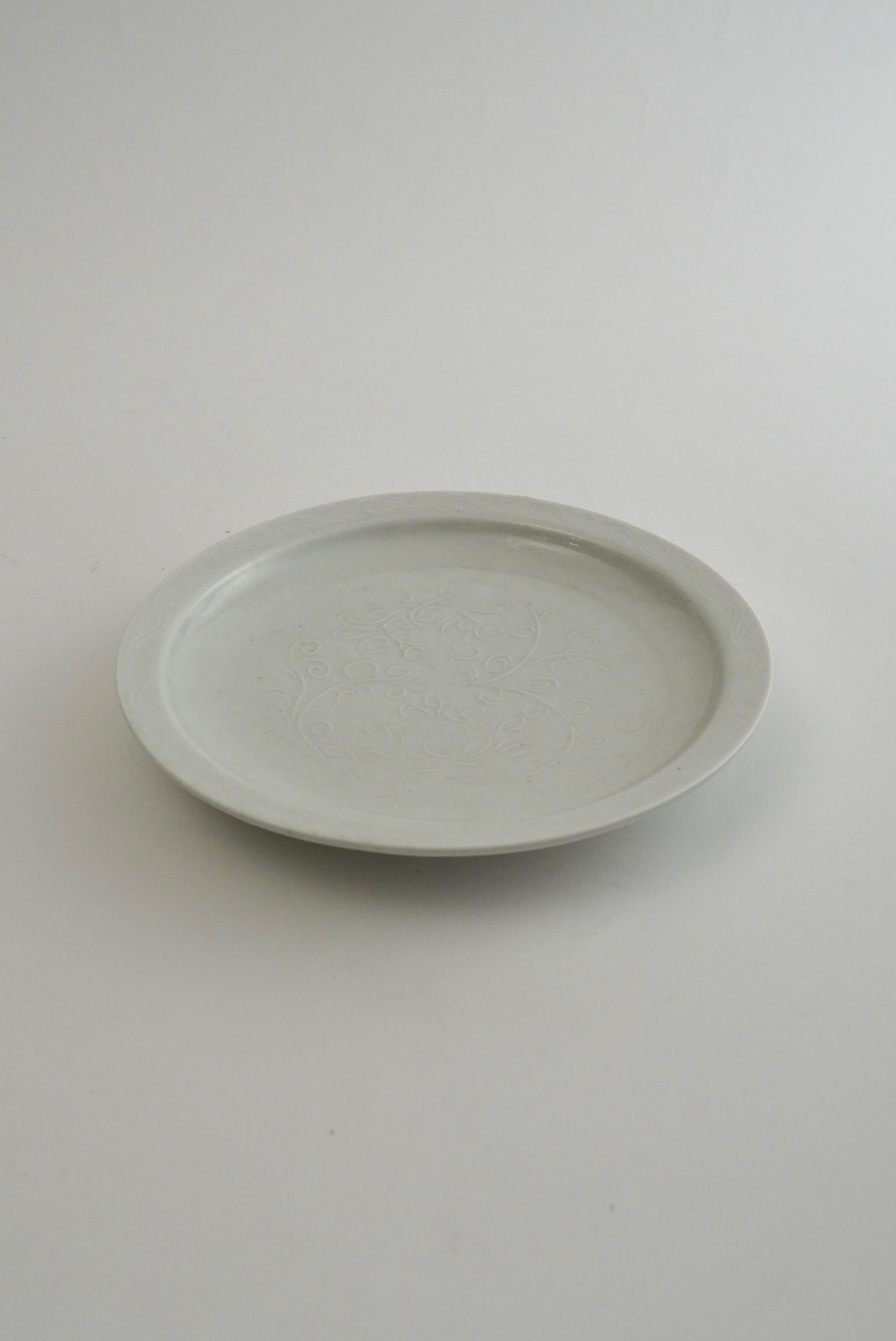 A round ceramic plate with a subtle textured glaze, photographed from a top-down perspective on a neutral light gray background.