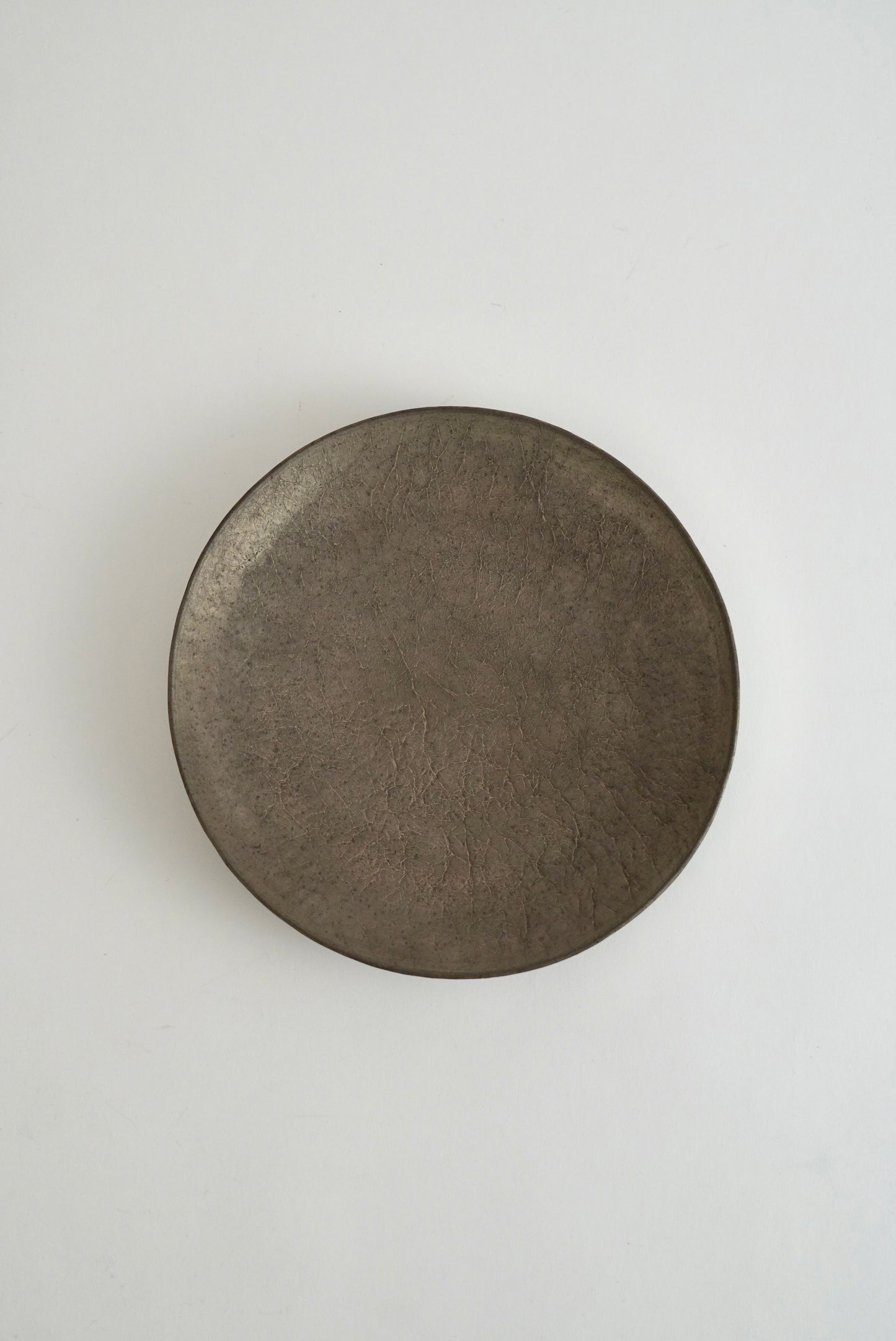A round, dark brown ceramic plate with a textured, matte finish, photographed from directly above on a clean, light off-white background.
