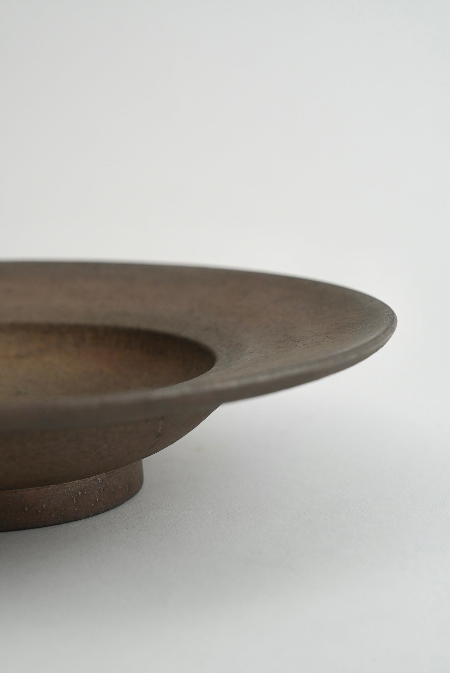 Close-up of a dark brown ceramic plate or shallow dish with a matte finish, showing the rim and base against a light gray background.