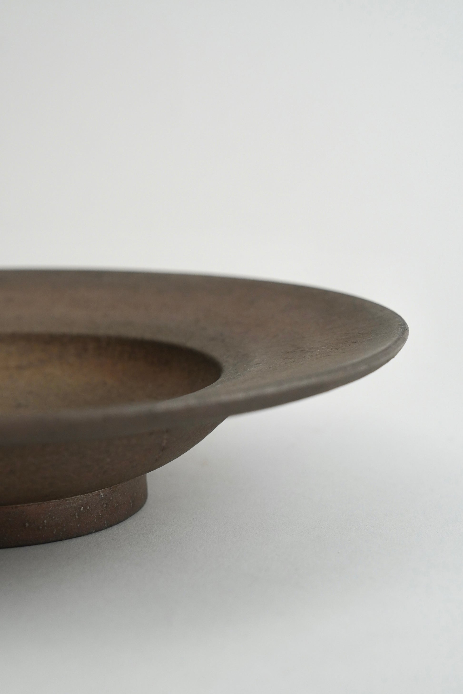 Close-up of a dark brown ceramic plate or shallow dish with a matte finish, showing the rim and base against a light gray background.