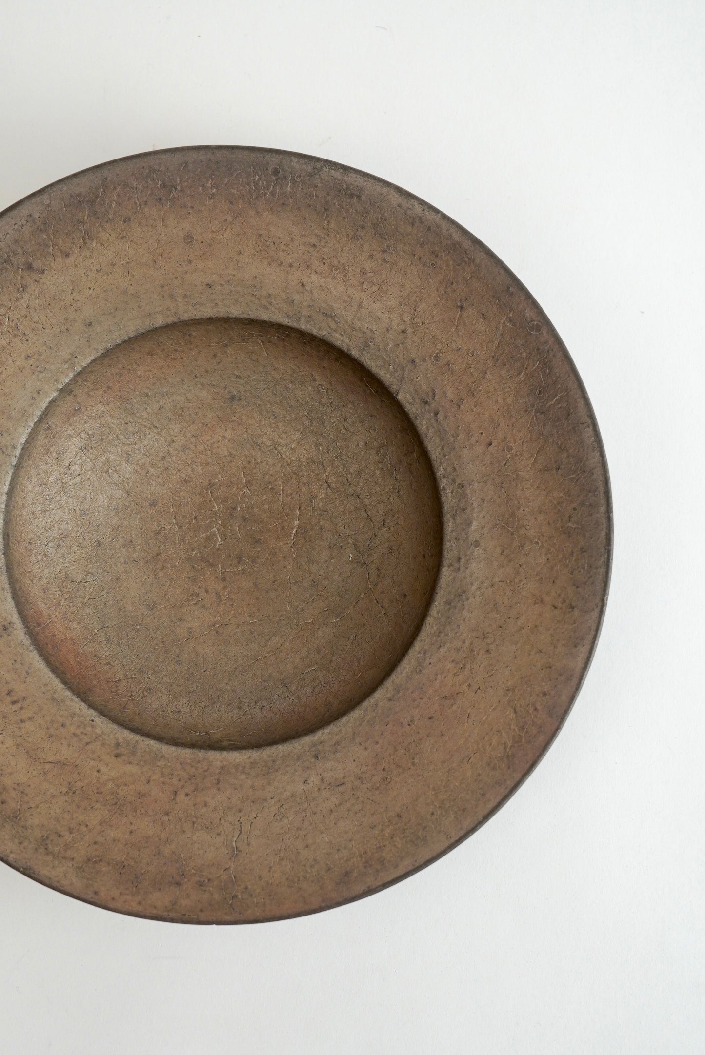 A rustic, round ceramic plate with a wide rim and a deep center, shown from a top-down perspective on a plain white background.