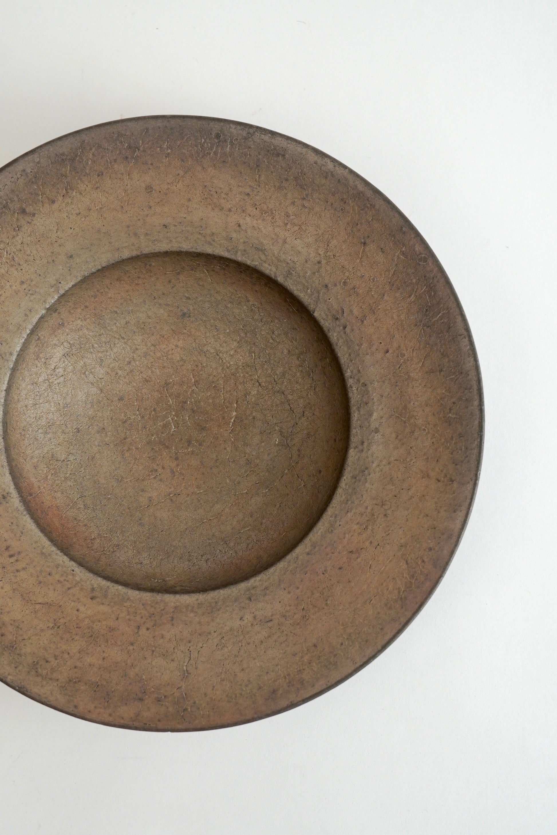 A rustic, round ceramic plate with a wide rim and a deep center, shown from a top-down perspective on a plain white background.