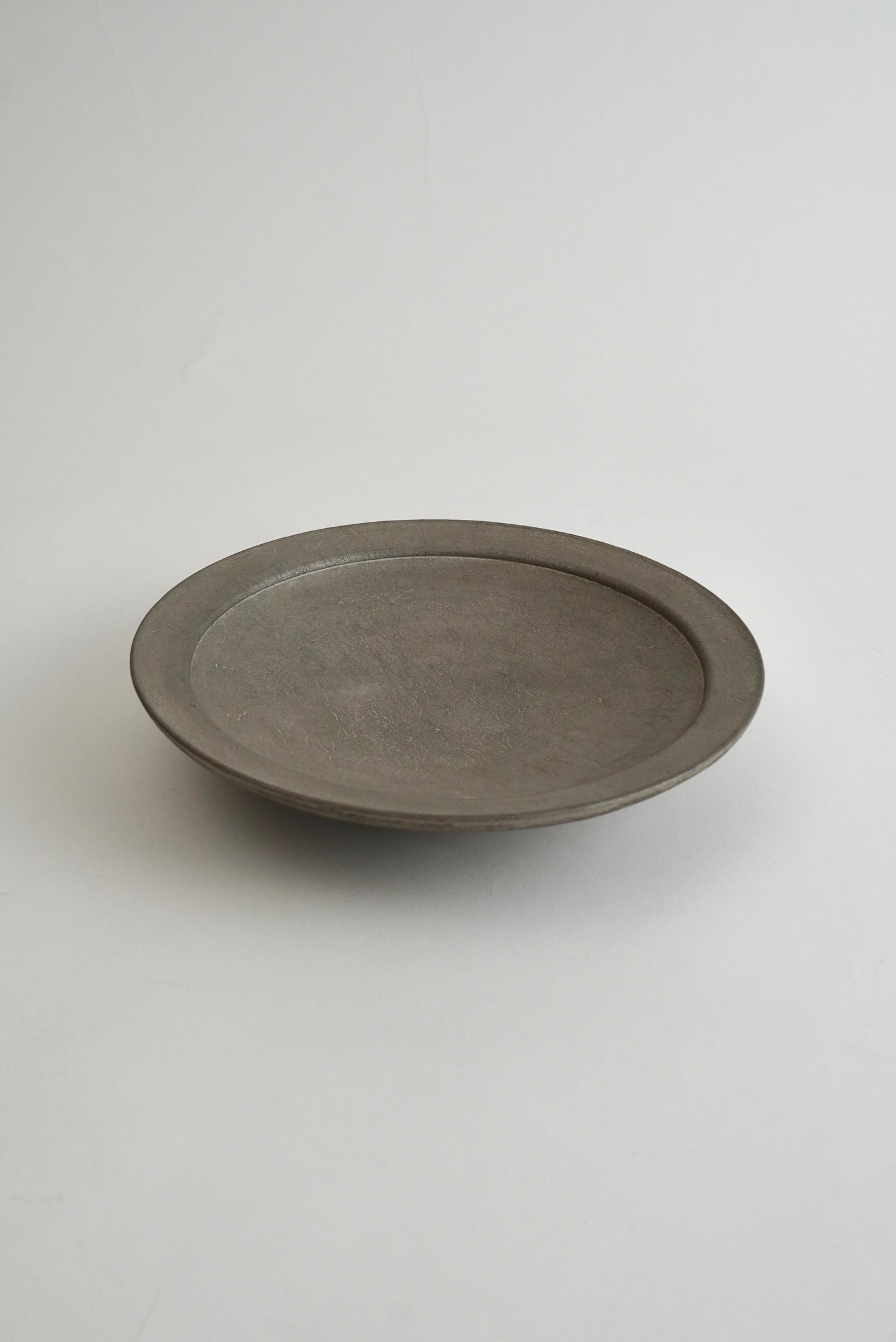 A minimalist, round gray ceramic plate with a shallow depth of profile, photographed on a seamless light gray background.