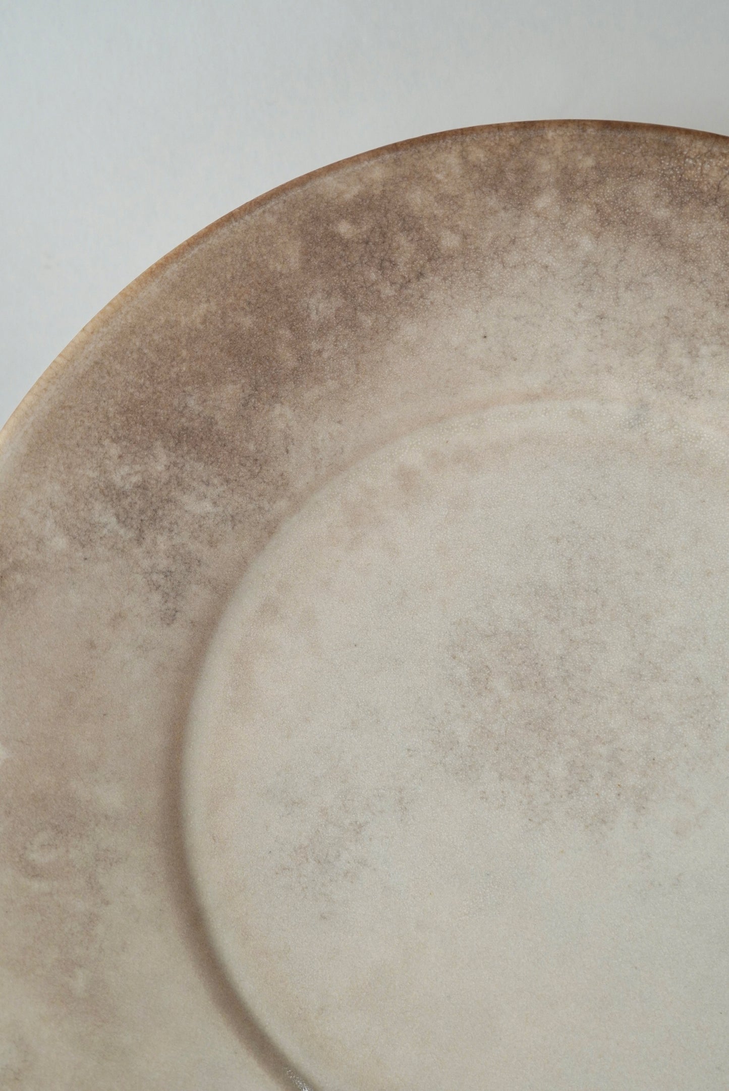 A close-up of a ceramic plate with a distressed, mottled finish in warm beige and brown tones.