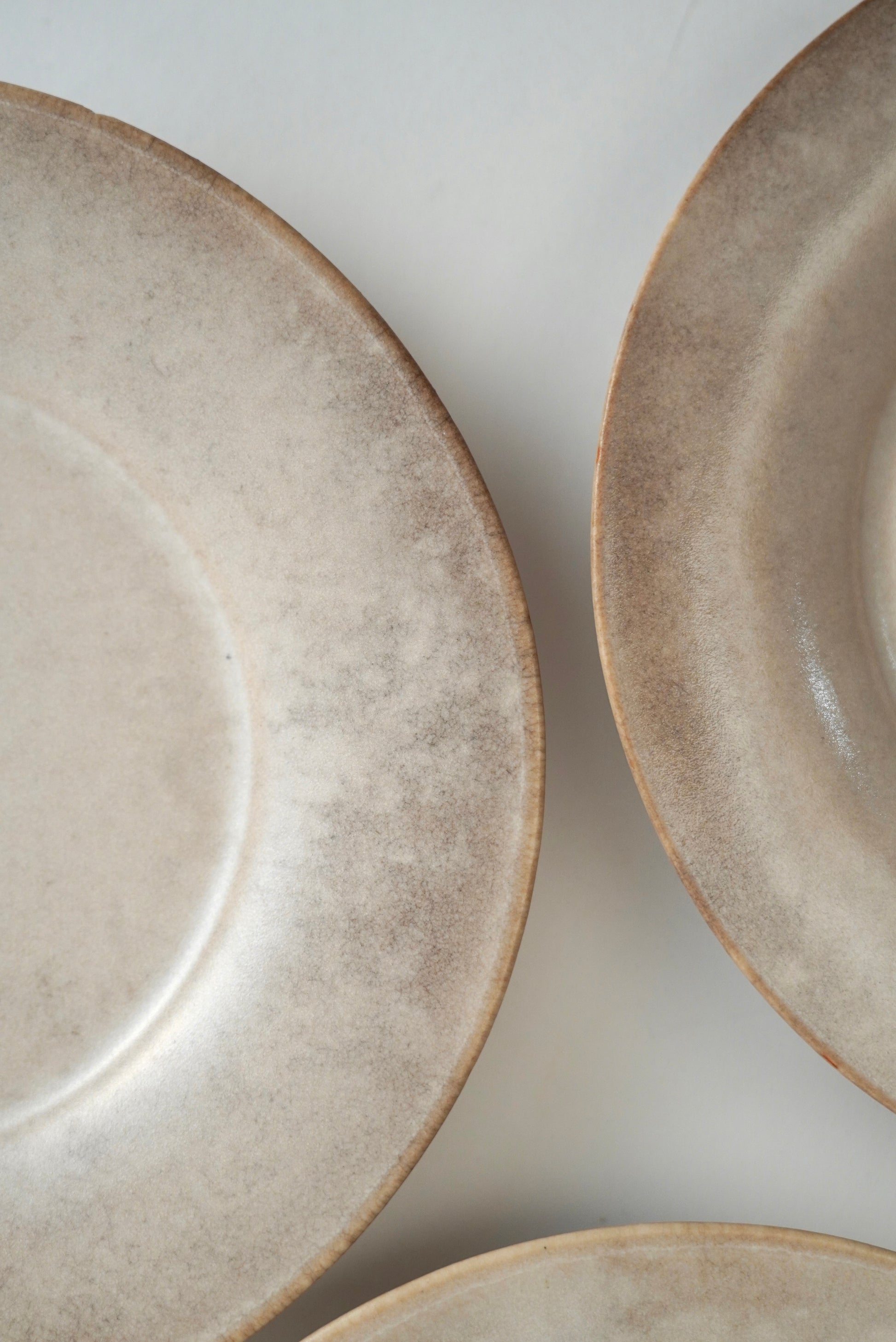 Close-up of ceramic plates with a textured, speckled beige and light brown glaze on a neutral off-white background.