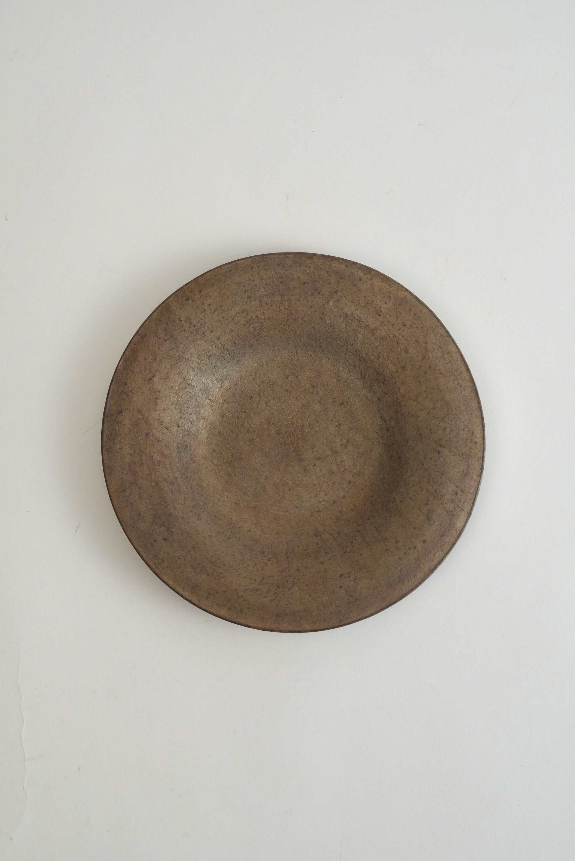 A round, shallow ceramic plate with a textured, matte finish in a dark brownish-gray glaze, photographed from directly above on a clean white background.