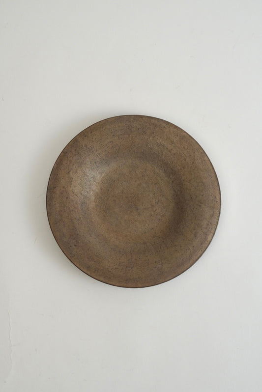 A round, shallow ceramic plate with a textured, matte finish in a dark brownish-gray glaze, photographed from directly above on a clean white background.