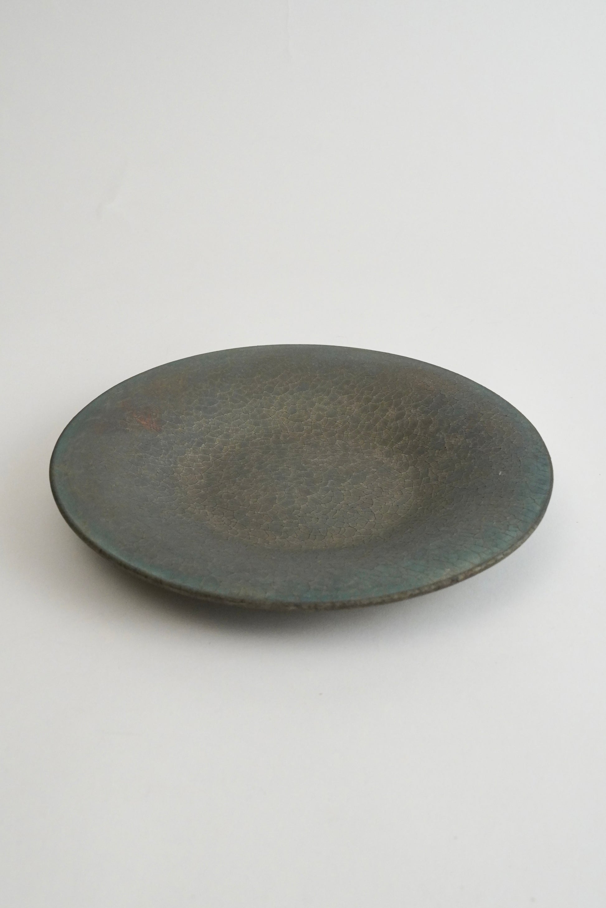 A round ceramic plate with a textured, matte finish in a dark gray-green glaze, photographed on a neutral light gray background.