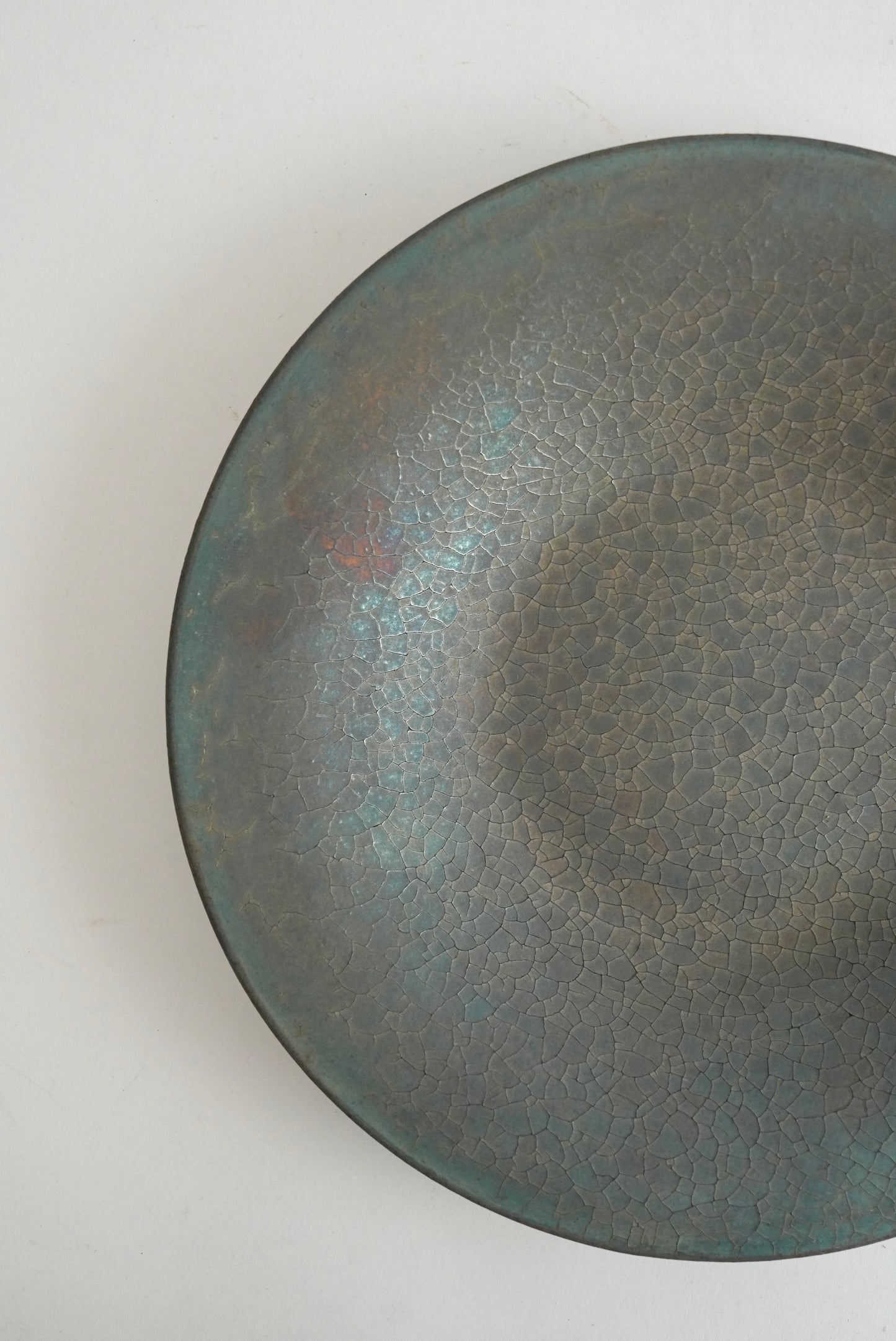 A close-up top-down view of a round ceramic bowl with a textured, crackled glaze in muted gray-green and blue-gray tones, set against a plain off-white background.