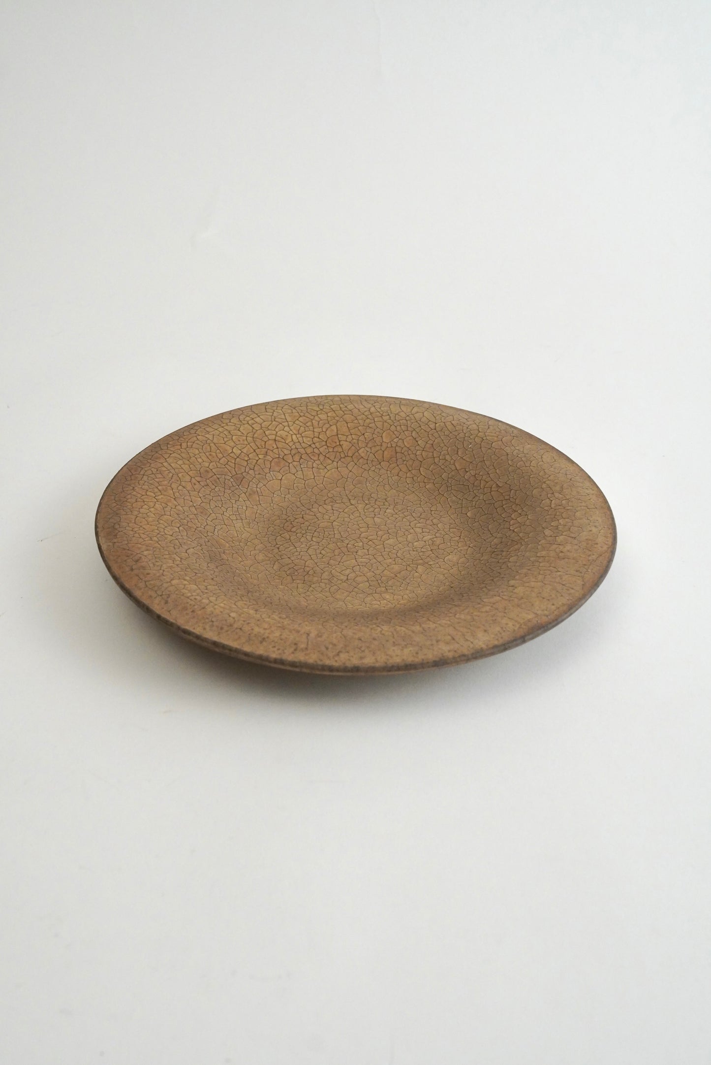 A round ceramic plate with a textured, speckled brown glaze, photographed from a top-down angle on a clean white background.