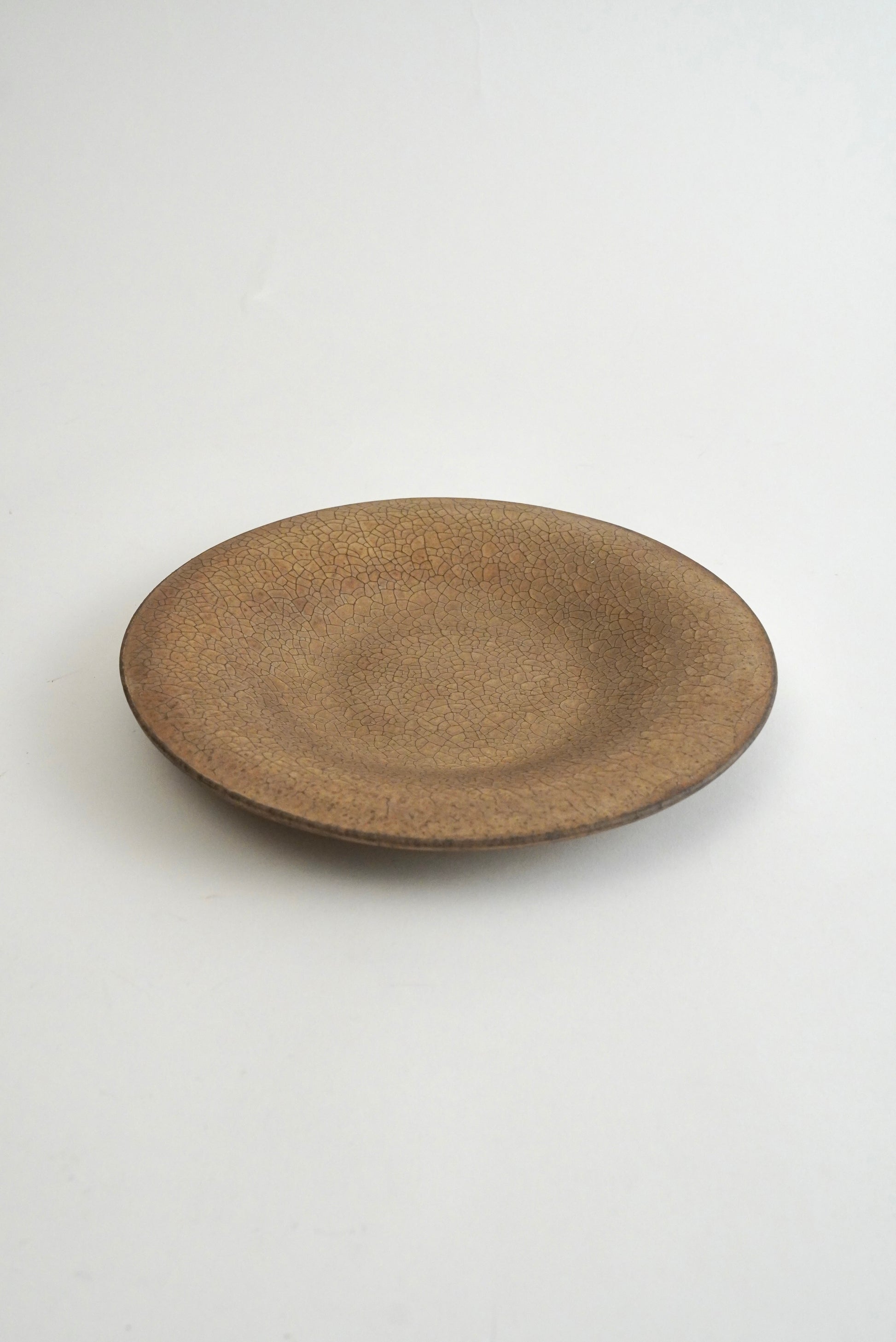 A round ceramic plate with a textured, speckled brown glaze, photographed from a top-down angle on a clean white background.