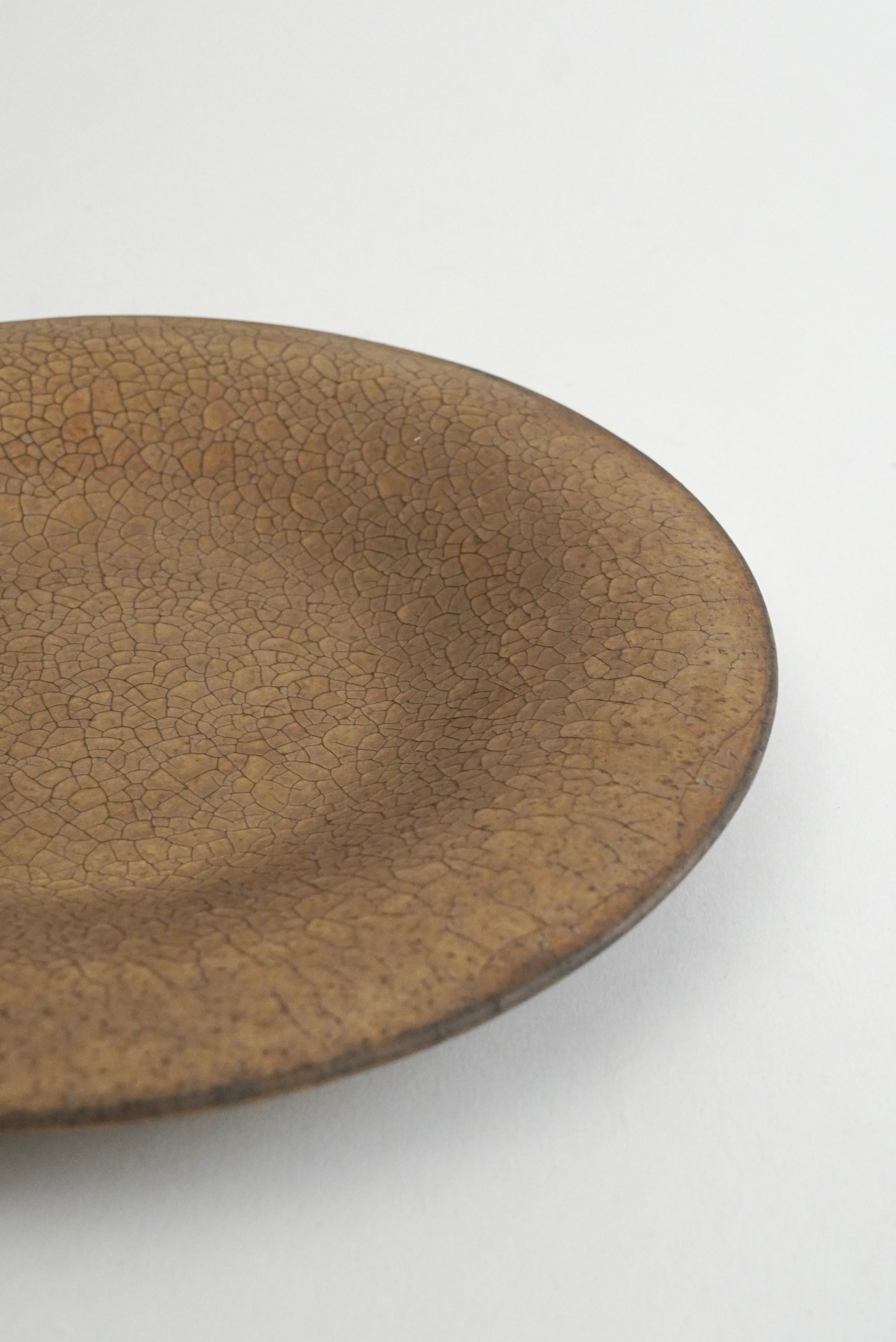 A close-up of a ceramic plate with a brown crackle glaze, showing its textured surface and shallow depth of field against a plain white background.