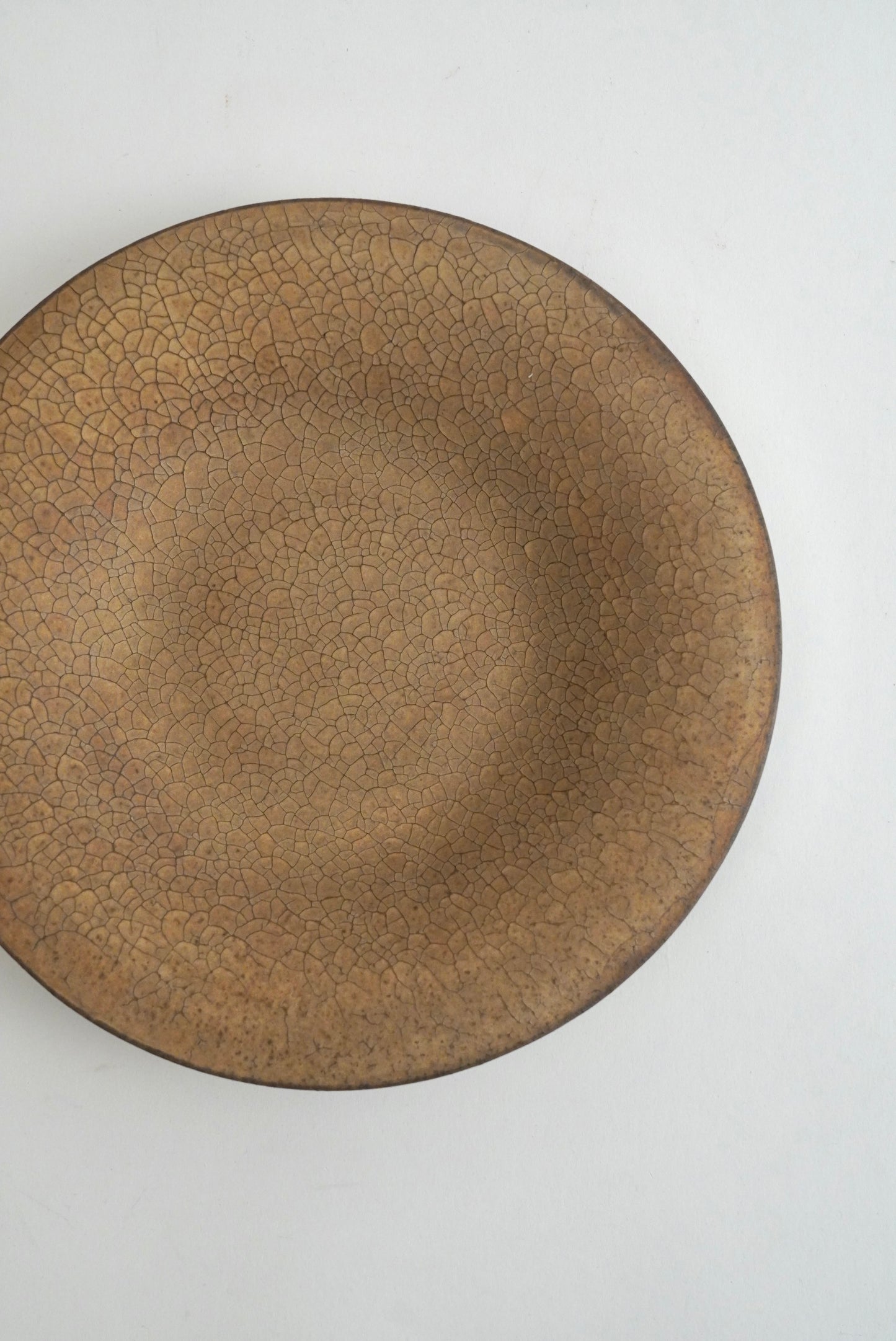 A round ceramic plate with a brown glaze featuring a distinctive crackle pattern, photographed from directly above on a plain white background.